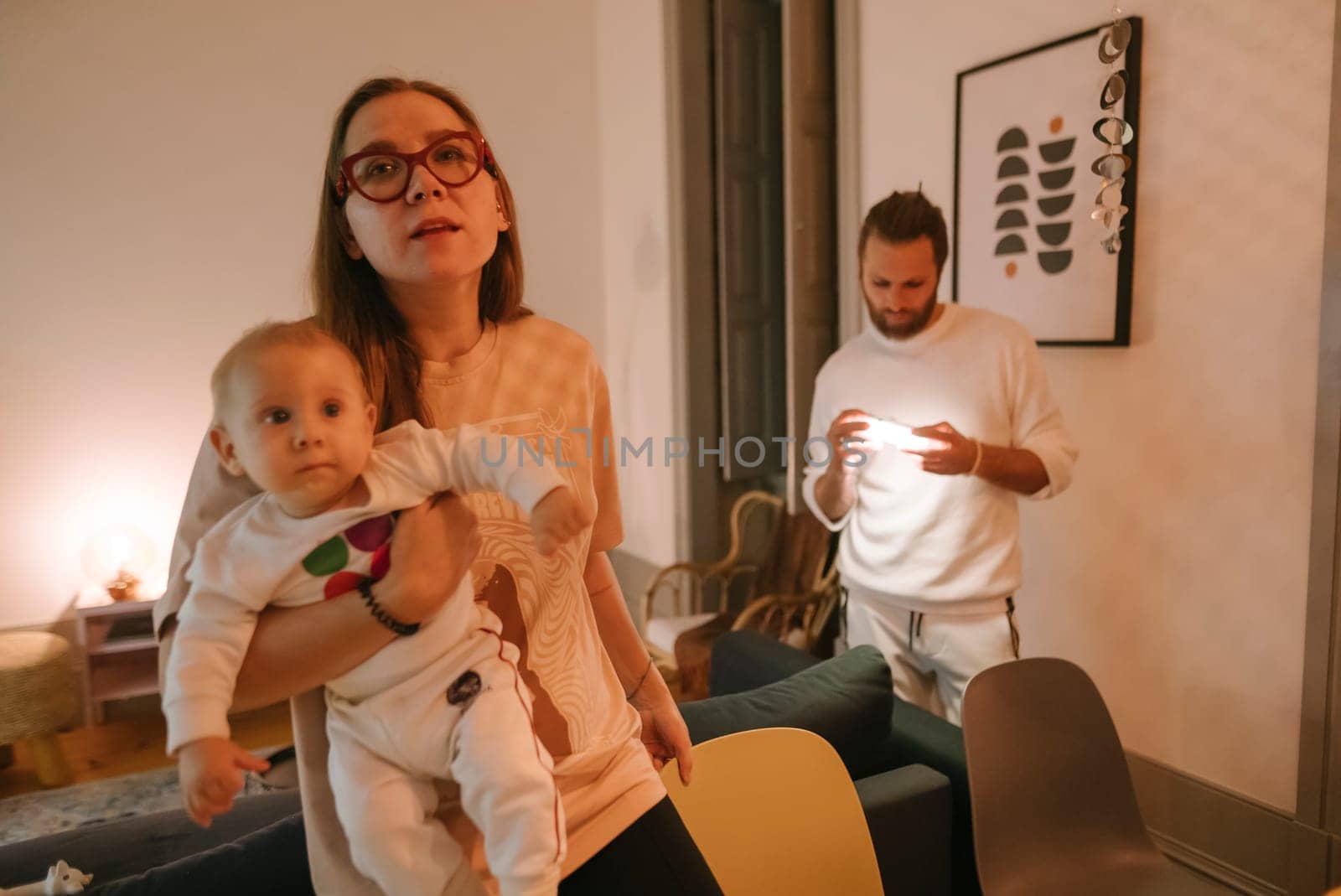 In a cozy and warm home setting, a loving mother gently holds her baby, while another adult engages with a phone