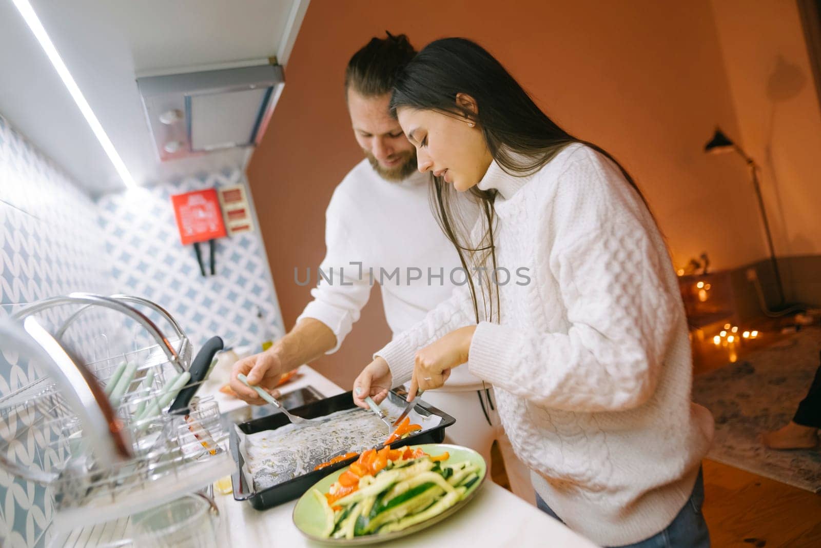 A couple is joyfully preparing a delicious meal together in their stylish and modern kitchen space full of life