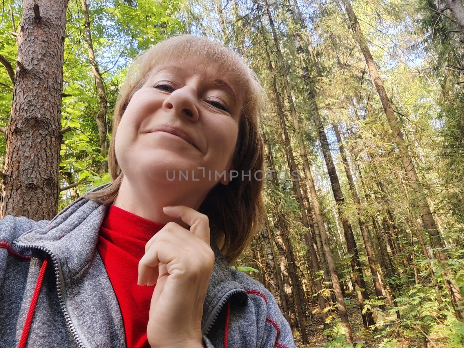 A middle-aged woman enjoys a delightful moment in a tranquil forest, capturing her smile while exploring nature.