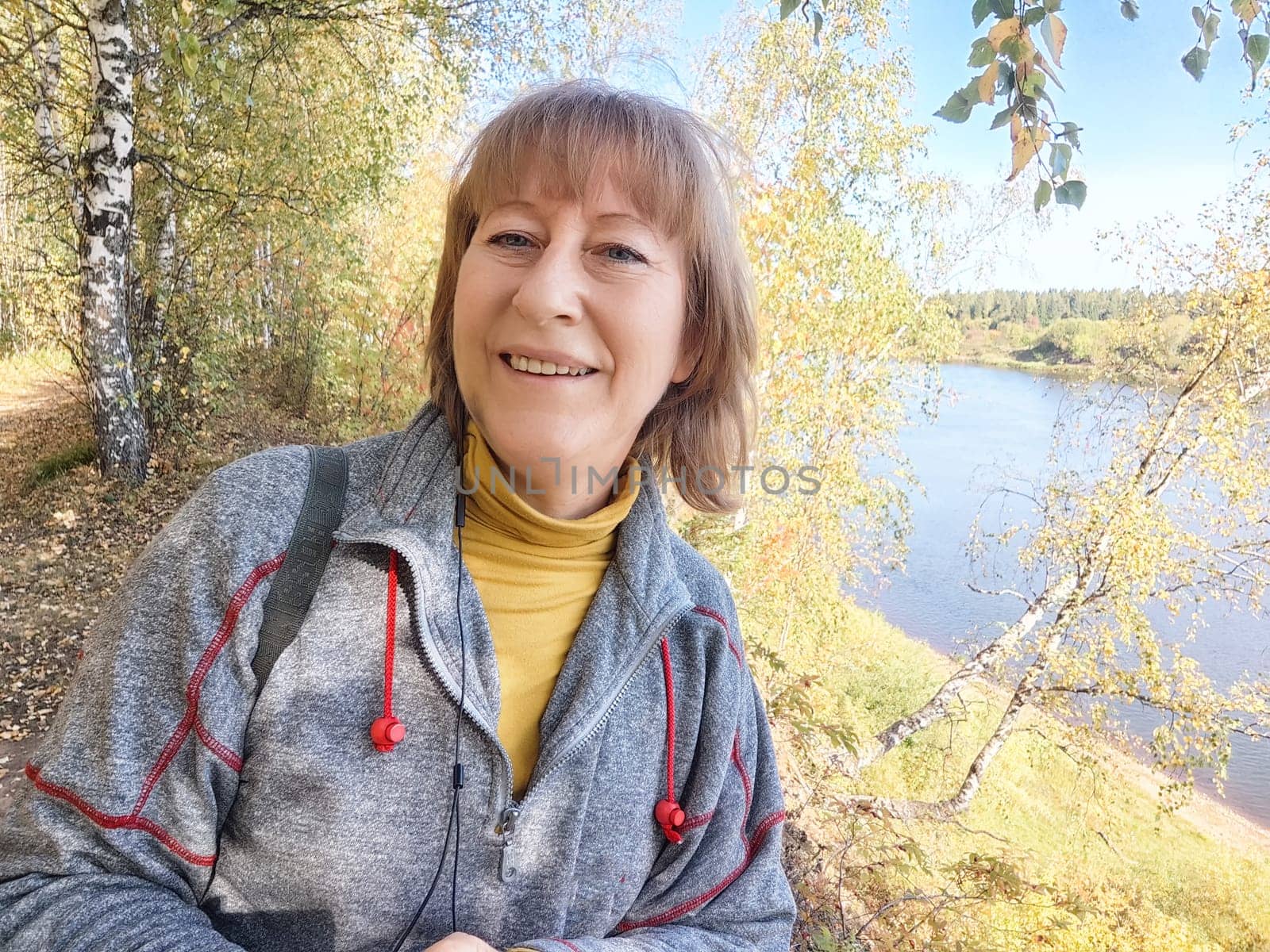 Woman smiling happily while exploring a scenic riverside in autumn, surrounded by colorful foliage and nature's beauty.