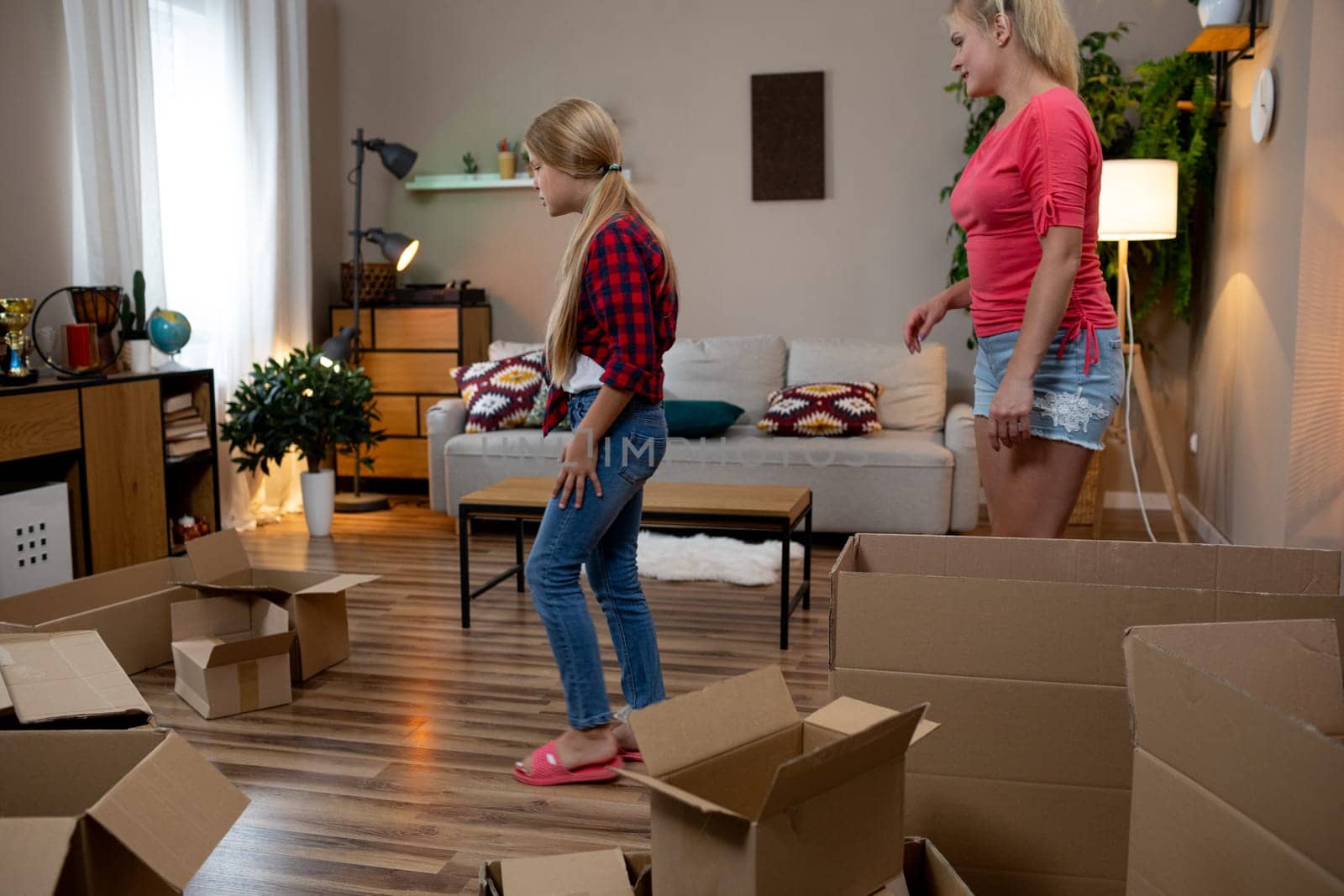 A cheerful young girl and a woman happily exploring their new home, filled with moving boxes all around them