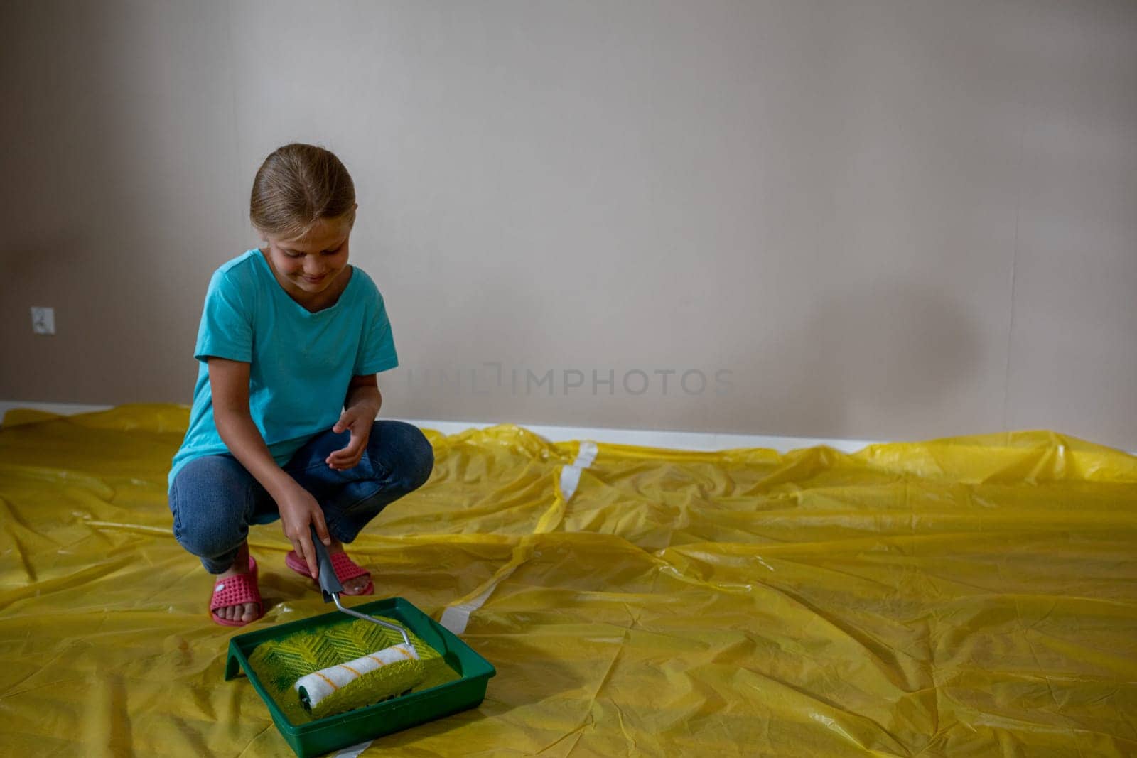 A young girl joyfully paints a room with a roller and tray, displaying her creativity in home improvement