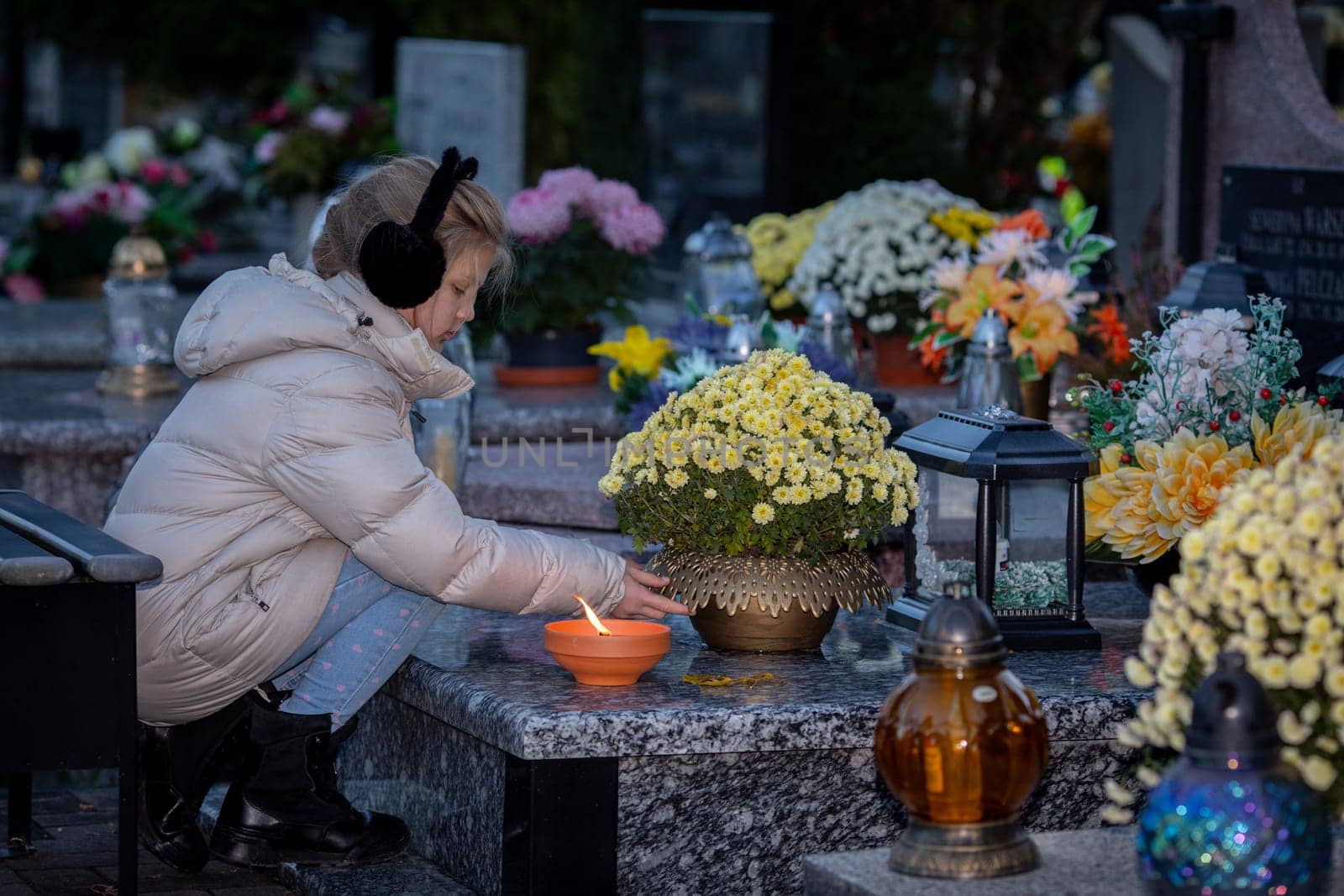 A young child gently places a flickering candle at a floweradorned grave, honoring and cherishing a sweet memory