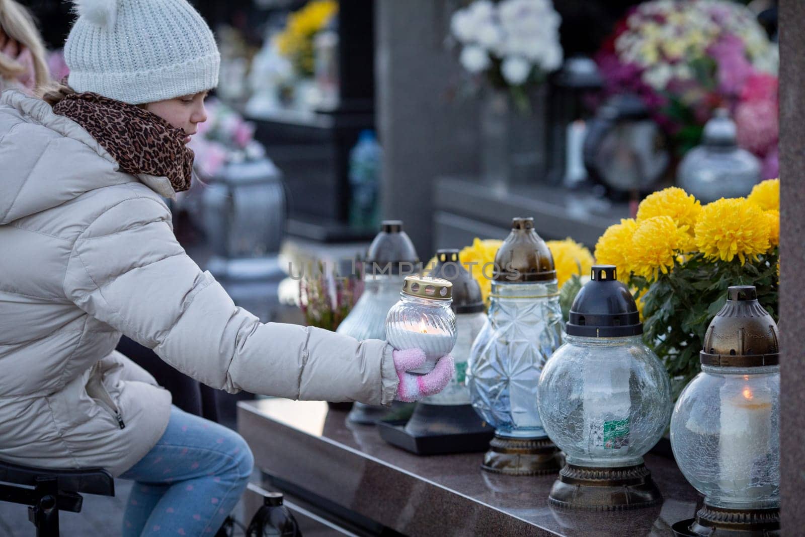 A solemn moment as someone lights lanterns in remembrance at a cemetery, surrounded by beautiful flowers