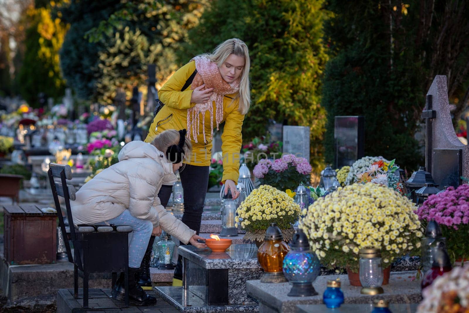Two individuals honor their departed loved ones with flowers and candles in a serene cemetery setting