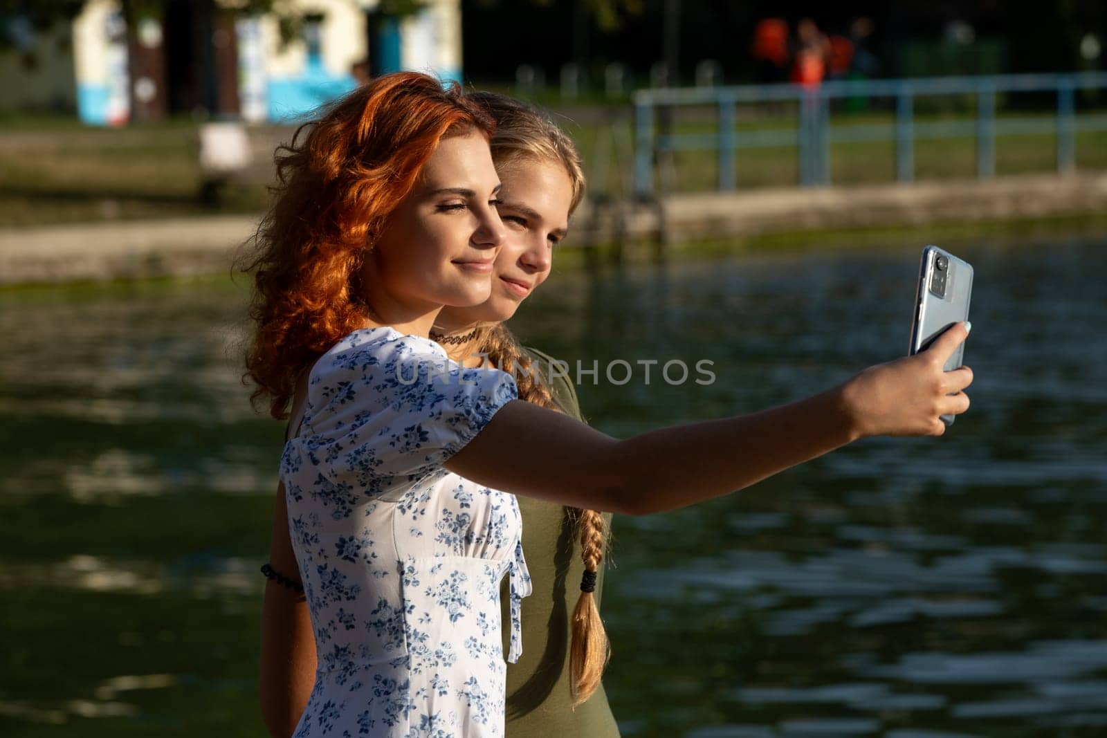 Two young women happily taking a selfie together by the serene lake, capturing a joyful moment in nature