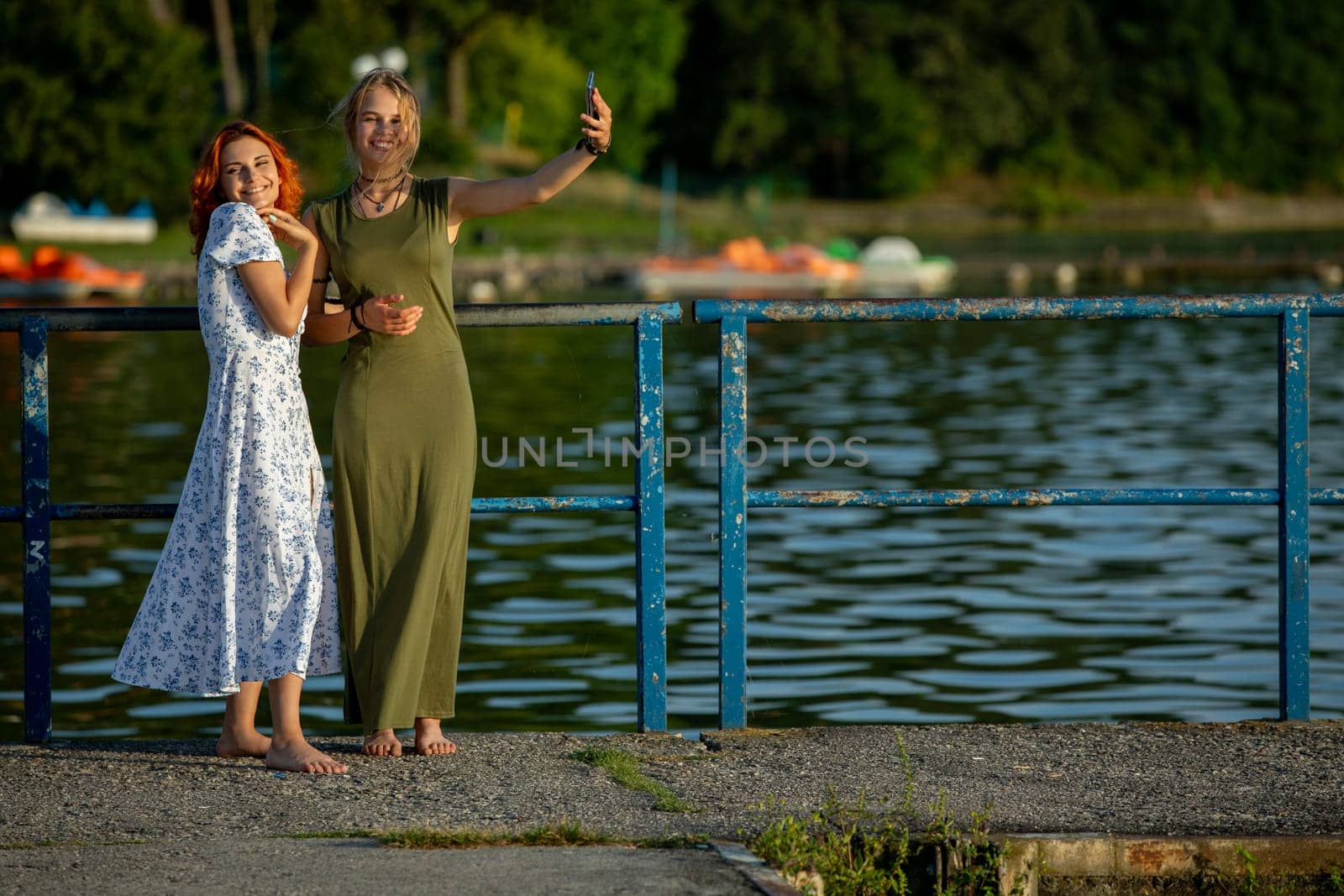 Two close friends joyfully pose by a serene lake, embracing cheerful summer vibes and enjoying their time together