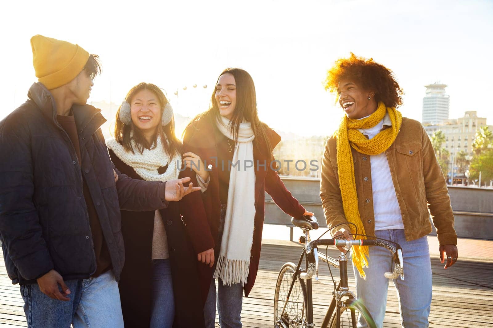 Group of happy multiracial friends laughing together while walking around city harbour on a sunny winter day. by Hoverstock