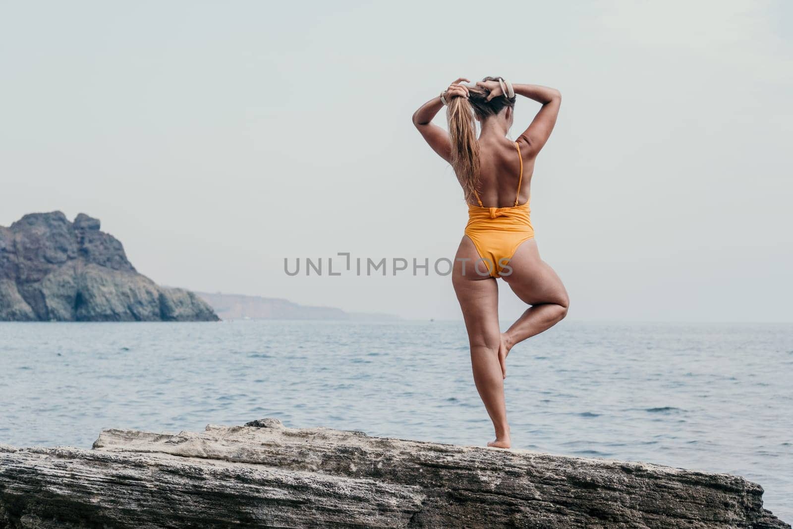 Woman sea yoga. Back view of free calm bliss satisfied woman with long hair standing on top rock with yoga position against of sky by the sea. Healthy lifestyle outdoors in nature, fitness concept. by panophotograph