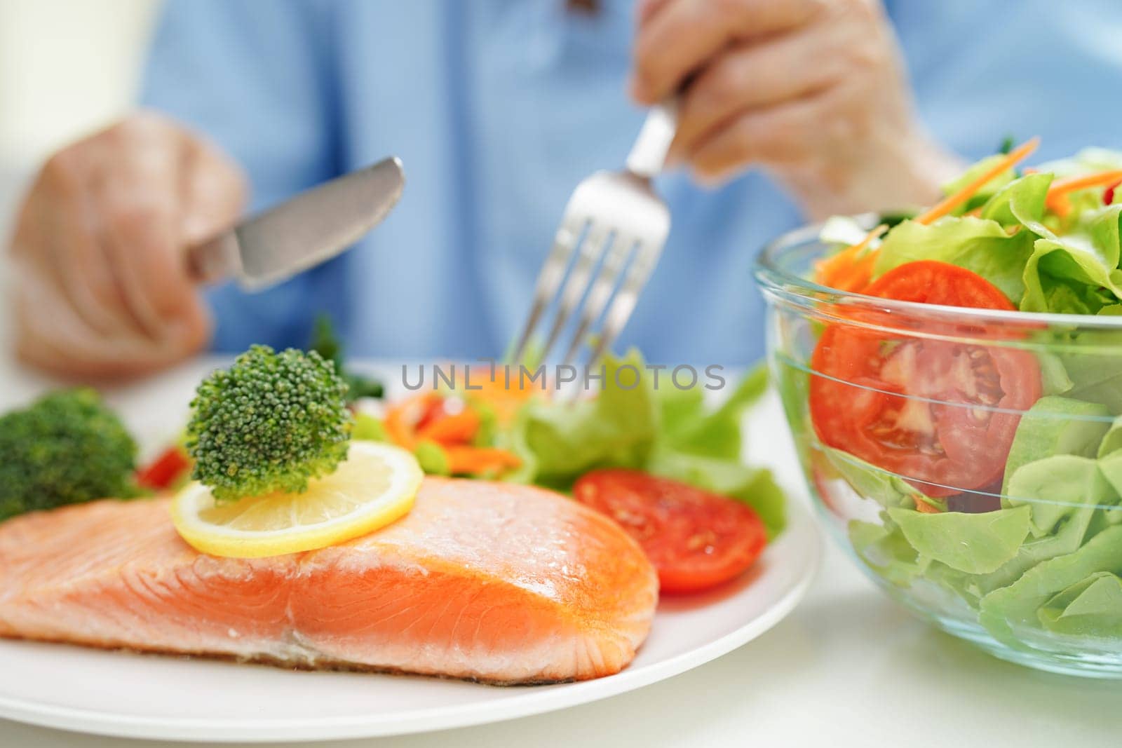 Asian elderly woman patient eating salmon stake and vegetable salad for healthy food in hospital.