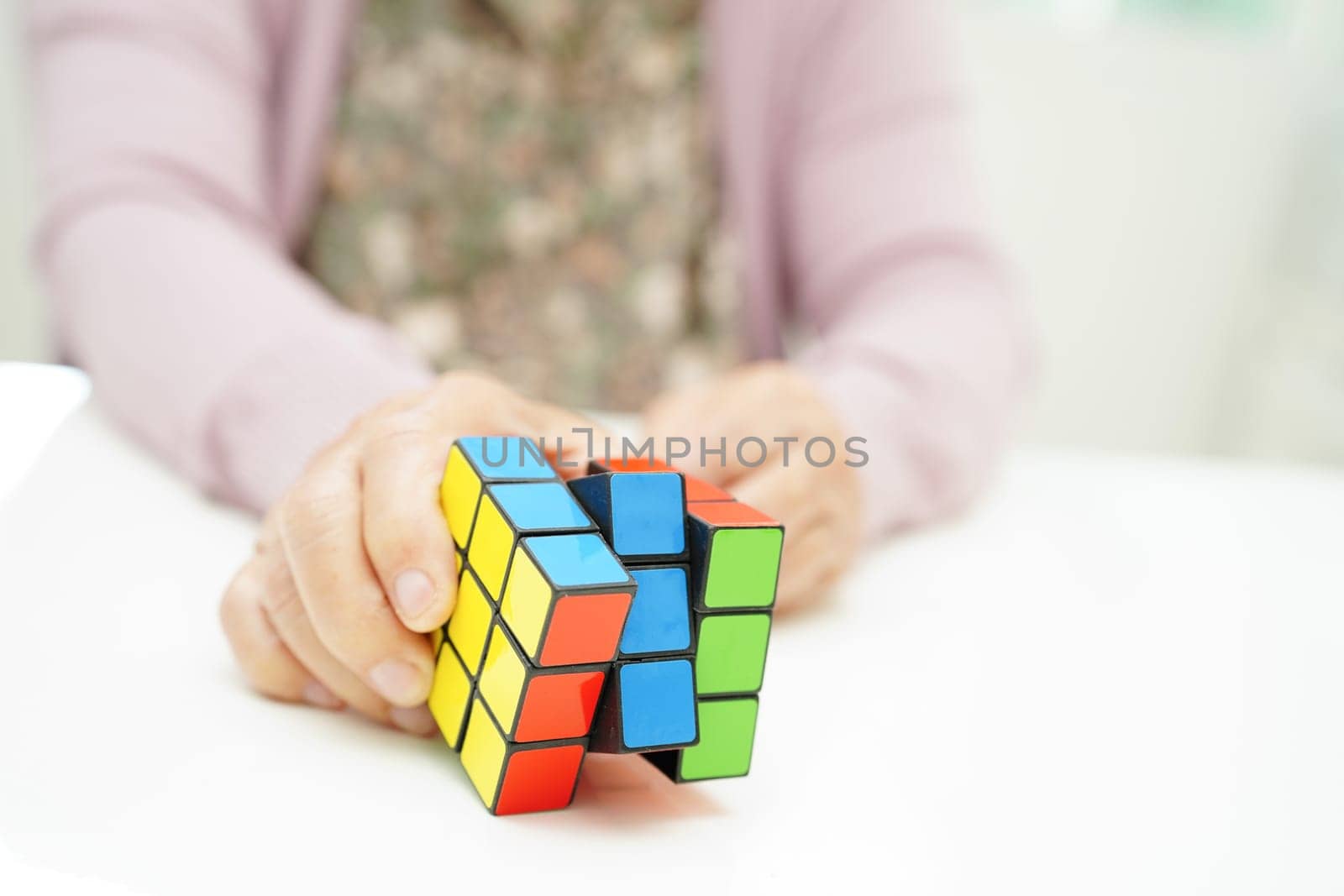 Bangkok, Thailand - May 15, 2022 Asian elderly woman playing Rubik cube game to practice brain training for help dementia prevention and Alzheimer disease.