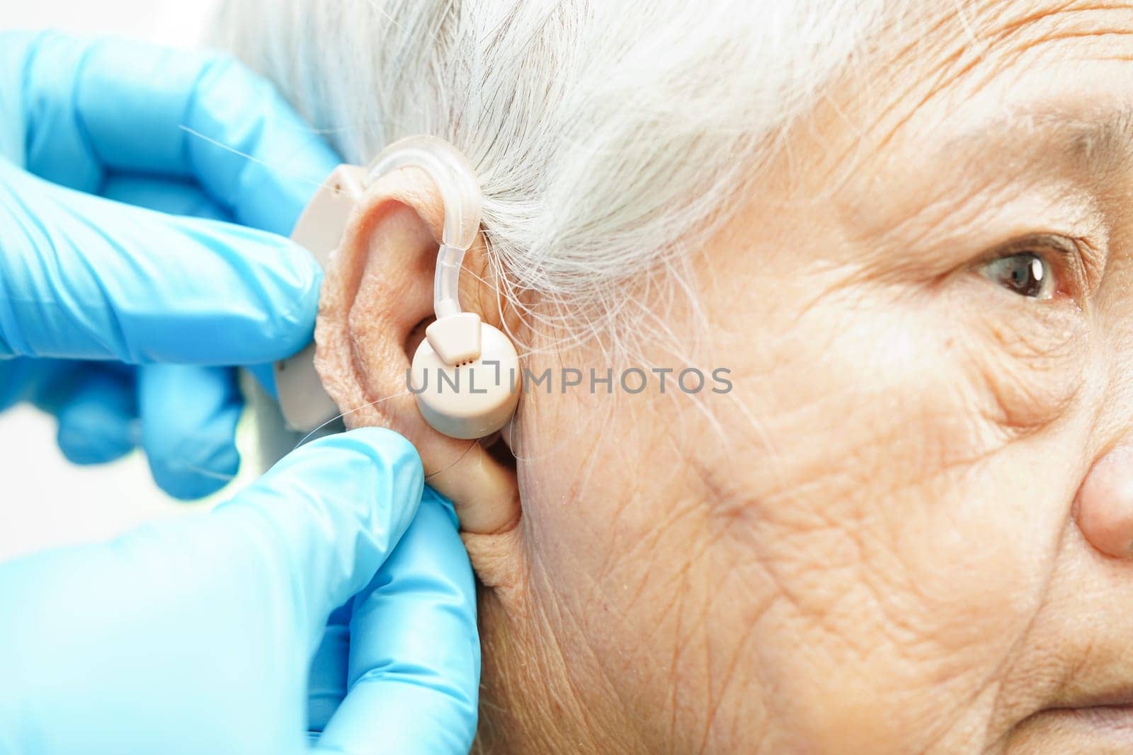 Doctor install hearing aid on senior patient ear to reduce hearing loss problem.