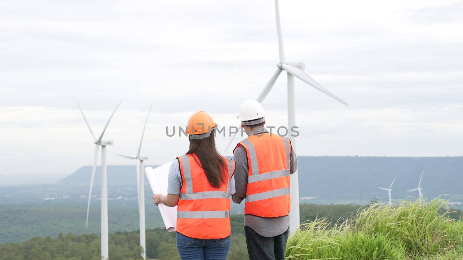 Male and female engineers working on a wind farm atop a hill or mountain in the rural. Progressive ideal for the future production of renewable, sustainable energy.