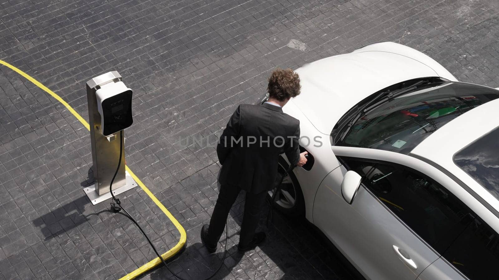 Progressive businessman unplugs charger plug from charging station to his electric car before driving around city center. Eco friendly rechargeable car powered by sustainable and clean energy.