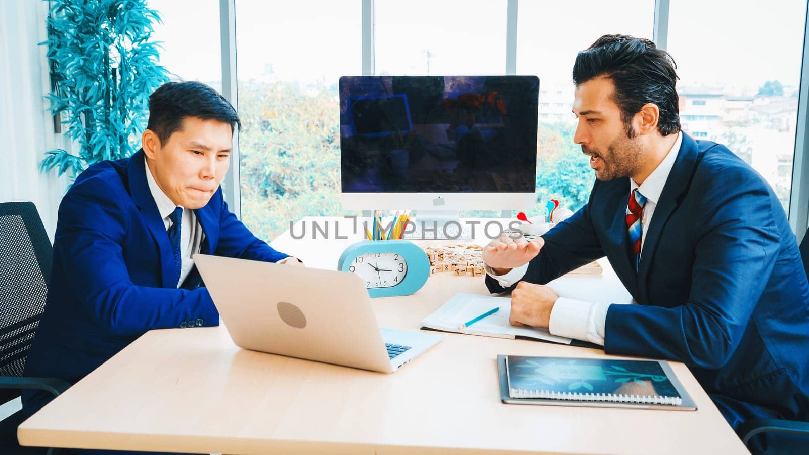 Two business people talk project strategy at office meeting room. Businessman discuss project planning with colleague at modern workplace while having conversation and advice on financial report. Jivy