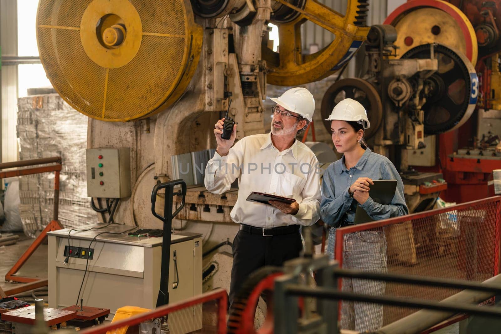 Factory engineer manager with assistant using laptop to conduct inspection of steel industrial machine, exemplifying leadership as machinery engineering inspection supervisor in metalwork manufacture.