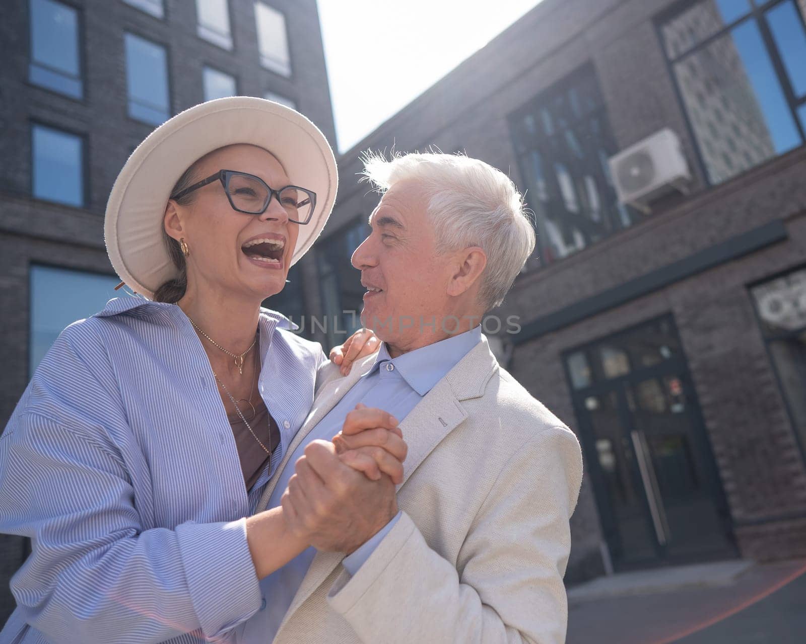 An elderly couple in love dances outdoors. A gray-haired man and a mature woman laugh and hug. by mrwed54