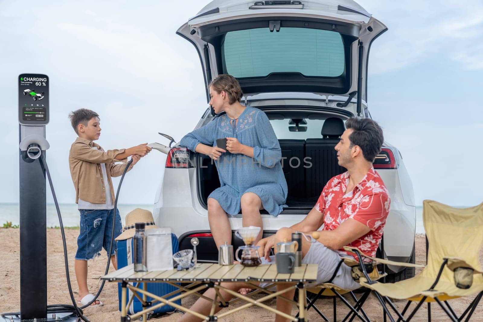 Family vacation trip traveling by the beach with electric car, happy family recharge EV car, enjoying outdoor camping coffee. Seascape travel and eco-friendly car for clean environment. Perpetual