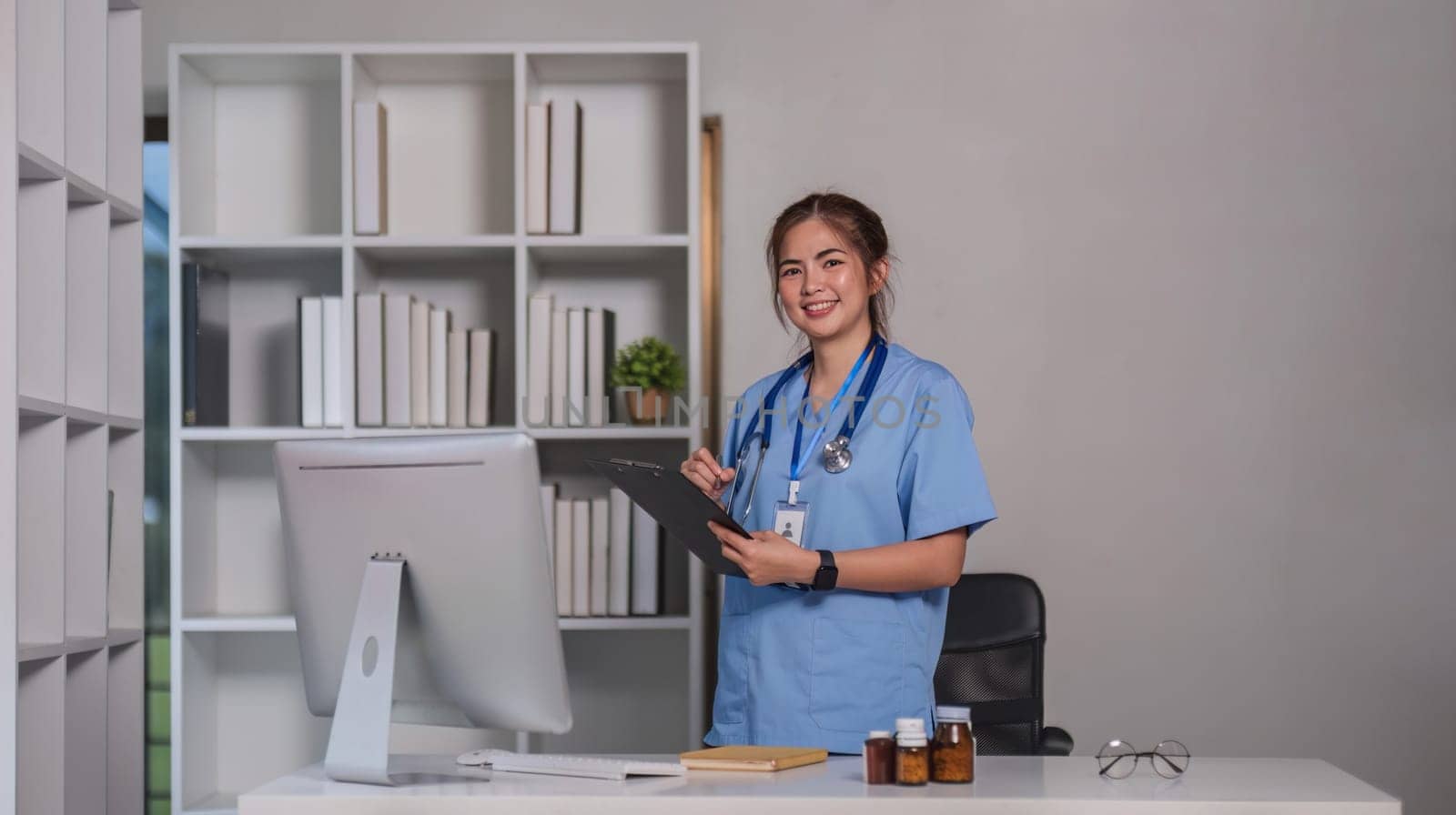 Young asian 30s female medic in uniform holding clipboard in doctor's office.