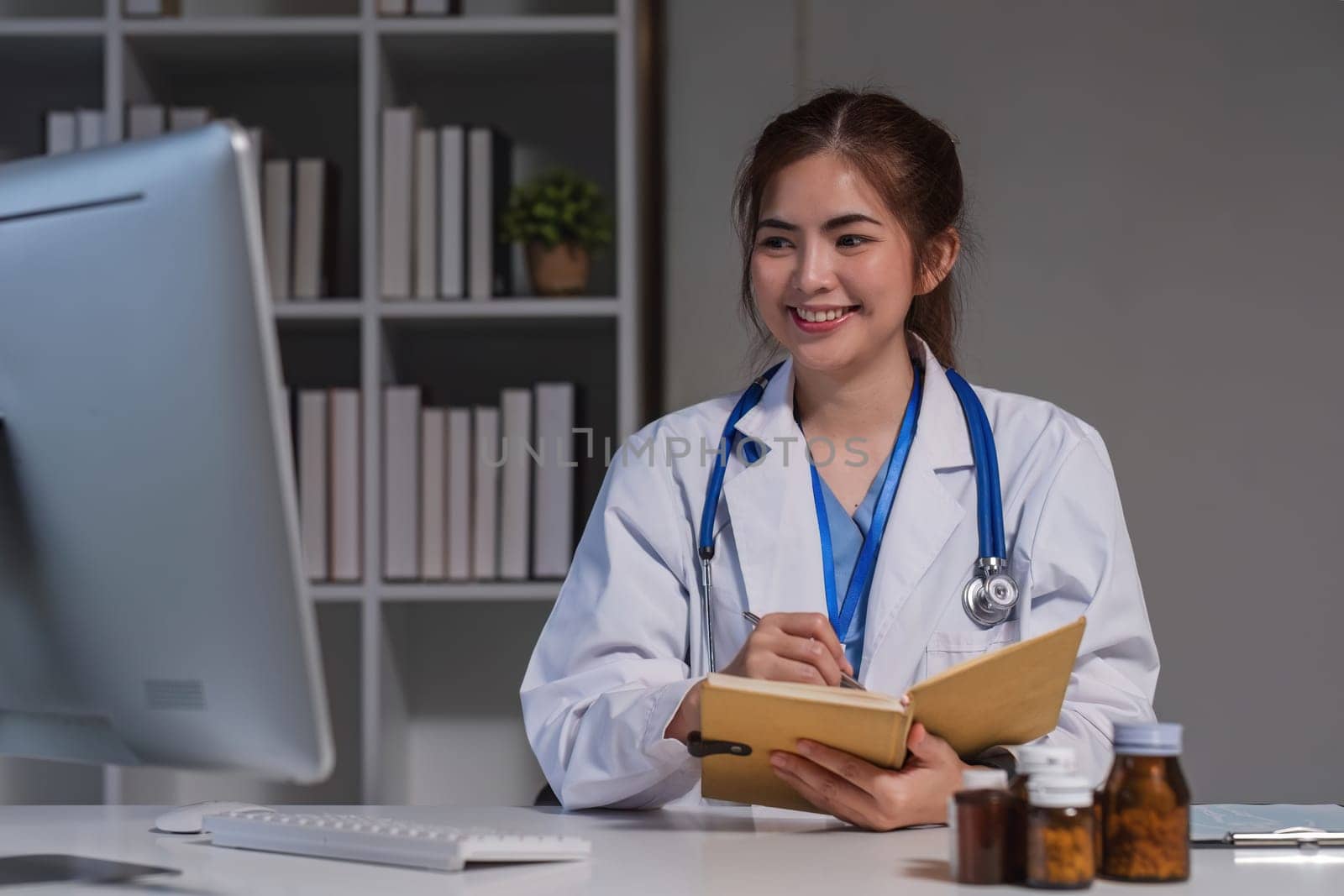 Asian female doctor, GP therapist in white coat writes prescription, sitting at prescription table, pharmaceutical concept..
