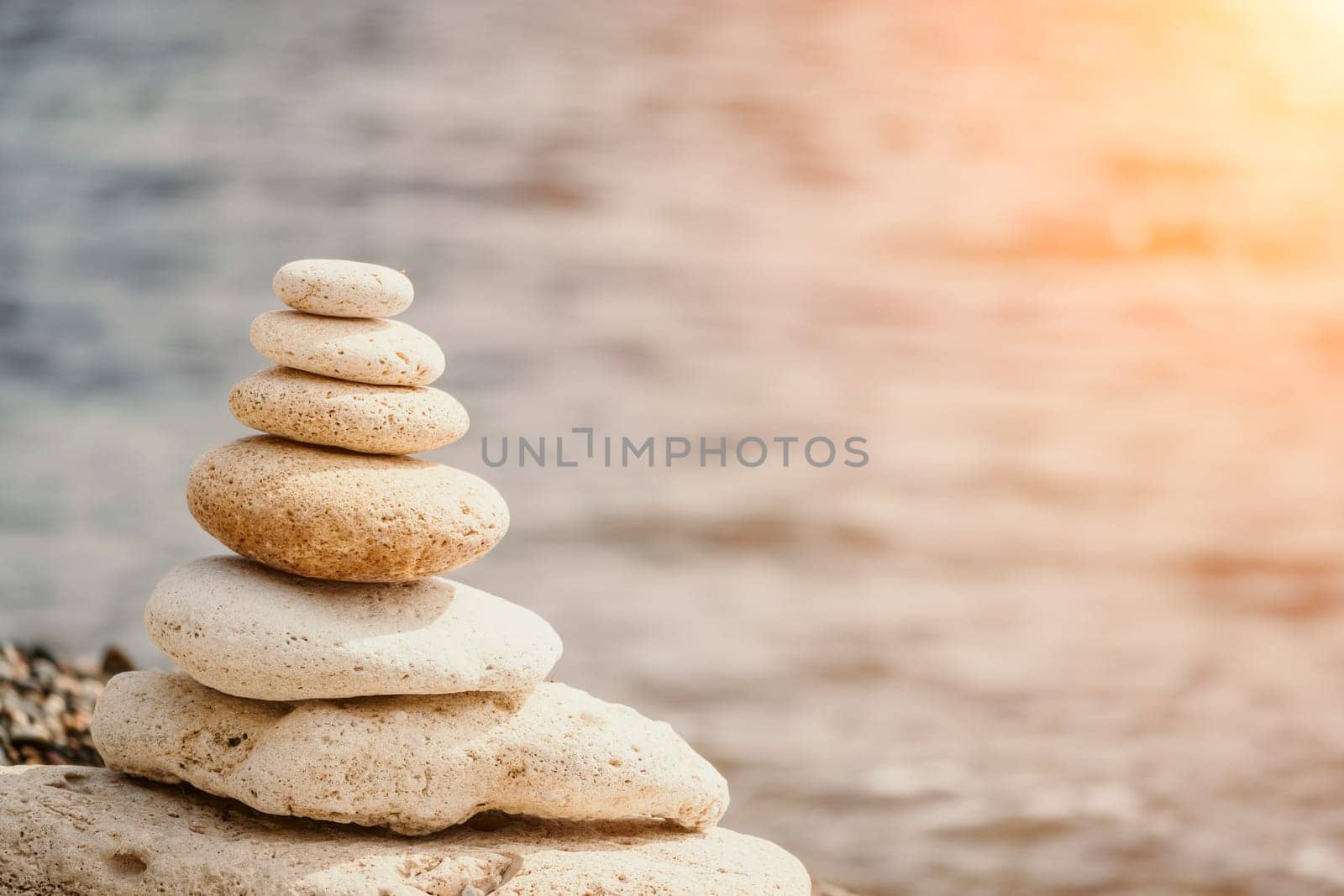 balanced rock pyramid on the pebbled beach is a study in harmony and balance. golden sea bokeh provide a stunning backdrop at sunset. Zen stones invite meditation and calm. spa or wellness concept. by panophotograph