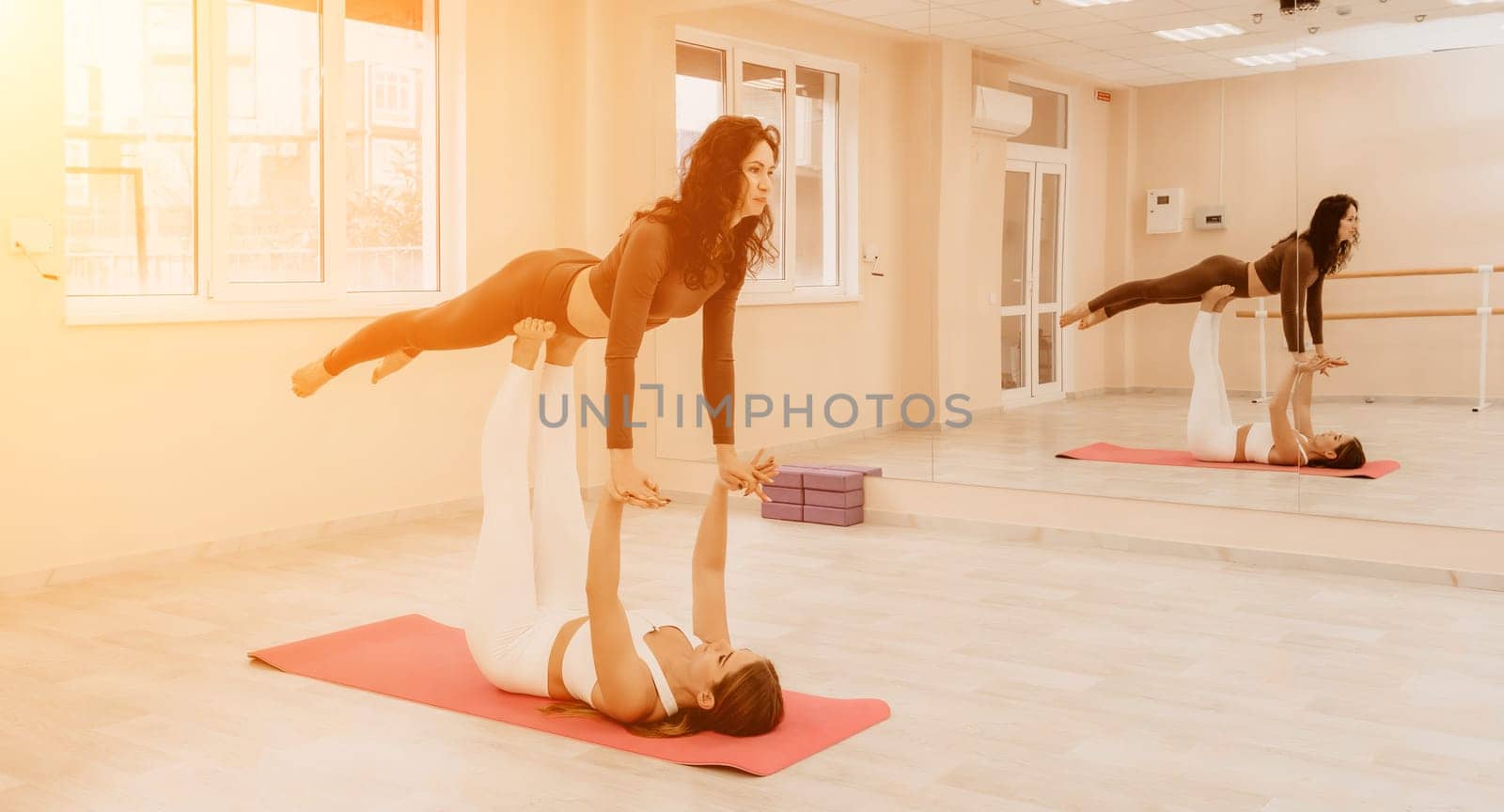 Two sporty women practicing yoga with advance posture. Young females in sportswear practices body balance and harmony together. Female fitness yoga partnership and unity concept. by panophotograph