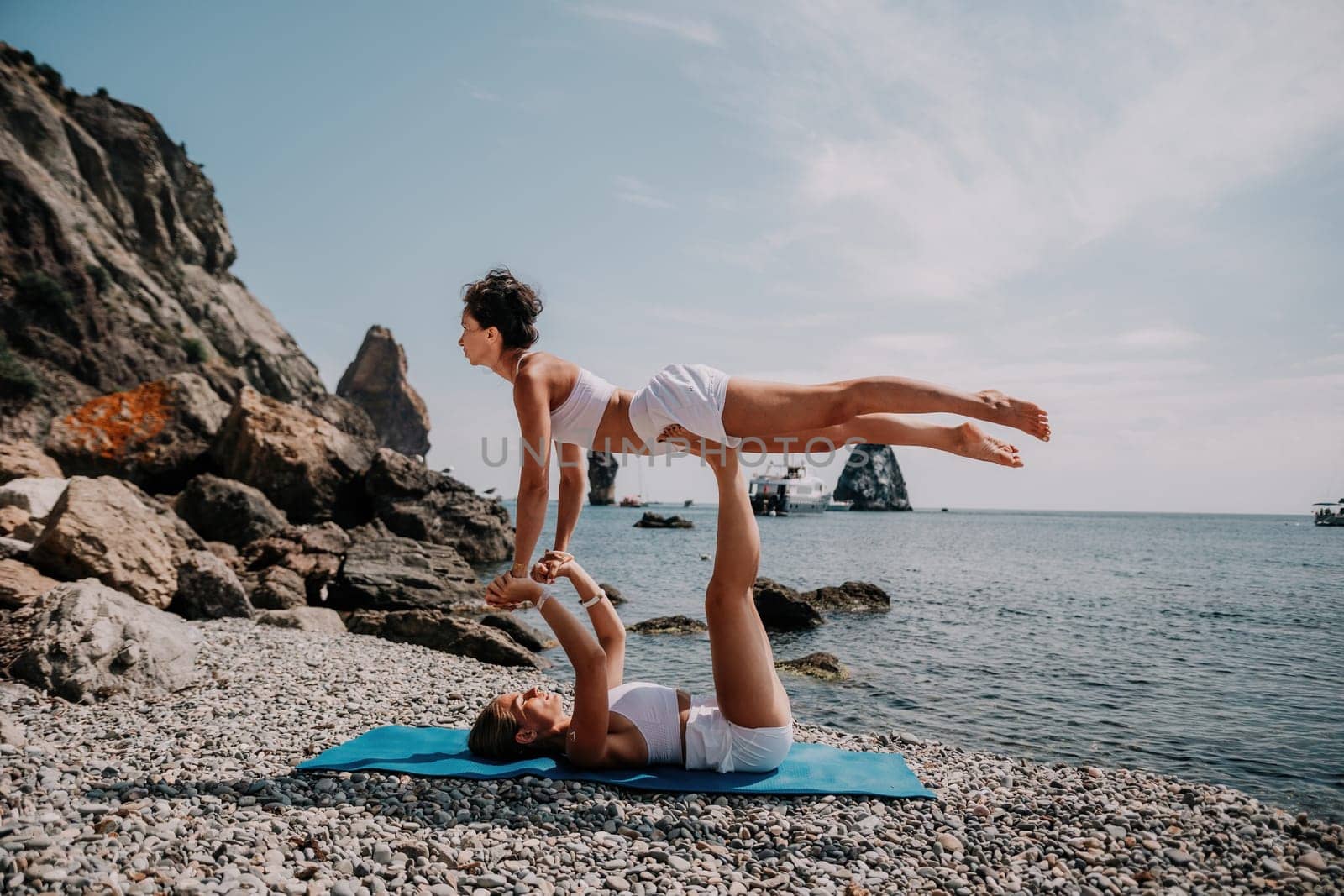 Woman sea yoga. Two Happy women meditating in yoga pose on the beach, ocean and rock mountains. Motivation and inspirational fit and exercising. Healthy lifestyle outdoors in nature, fitness concept. by panophotograph