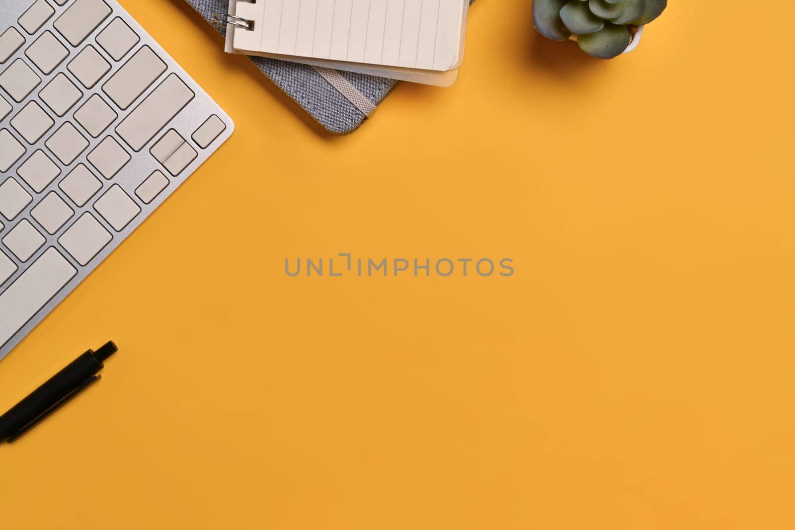 Top view keyboard, notebook and succulent plant on yellow background. Space for text advertising text message.