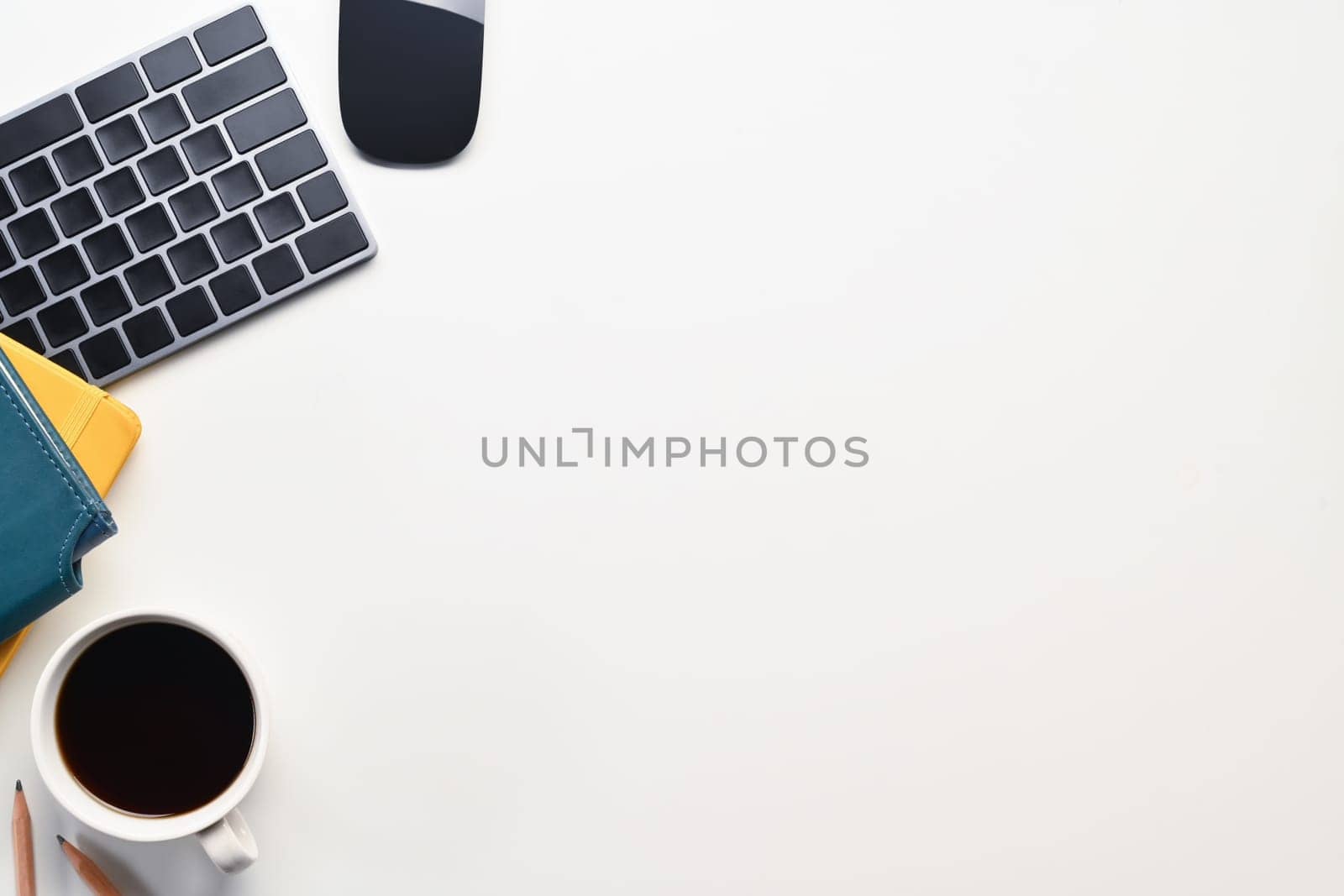 A coffee cup, notebooks, keyboard and mouse on white table. Space for text advertising text message.