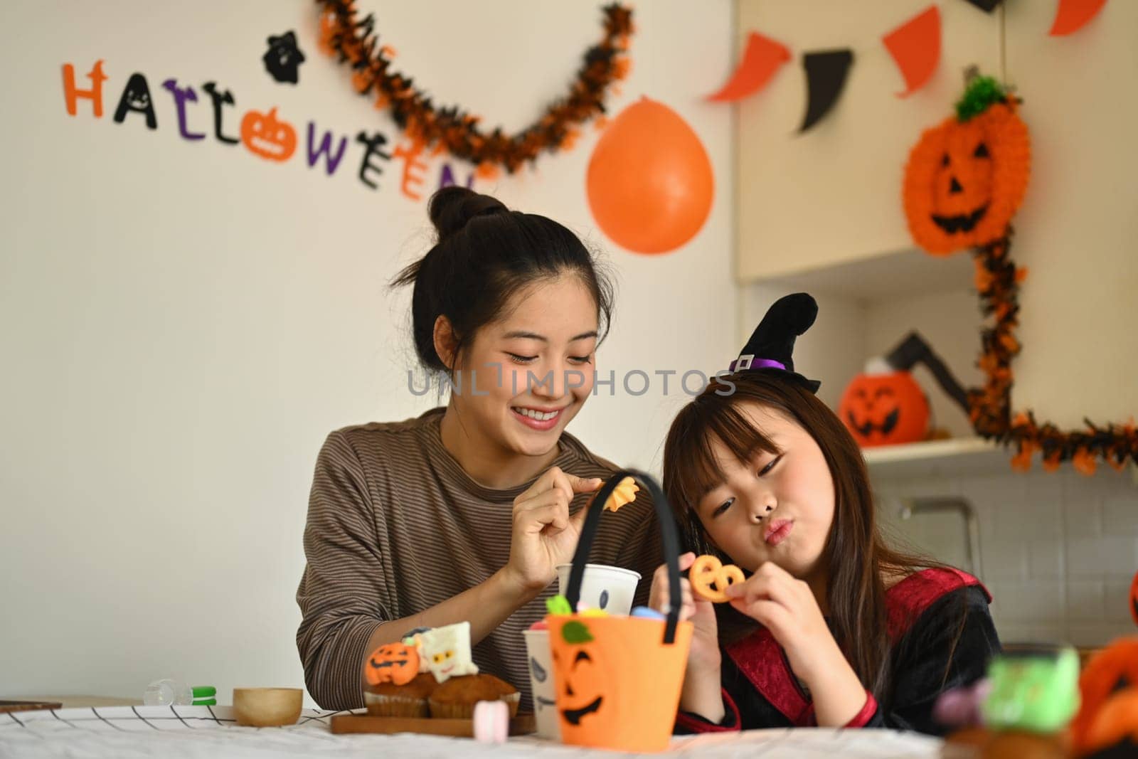 Smiling young mother and her little daughter getting ready for the holiday, making Halloween cupcakes by prathanchorruangsak