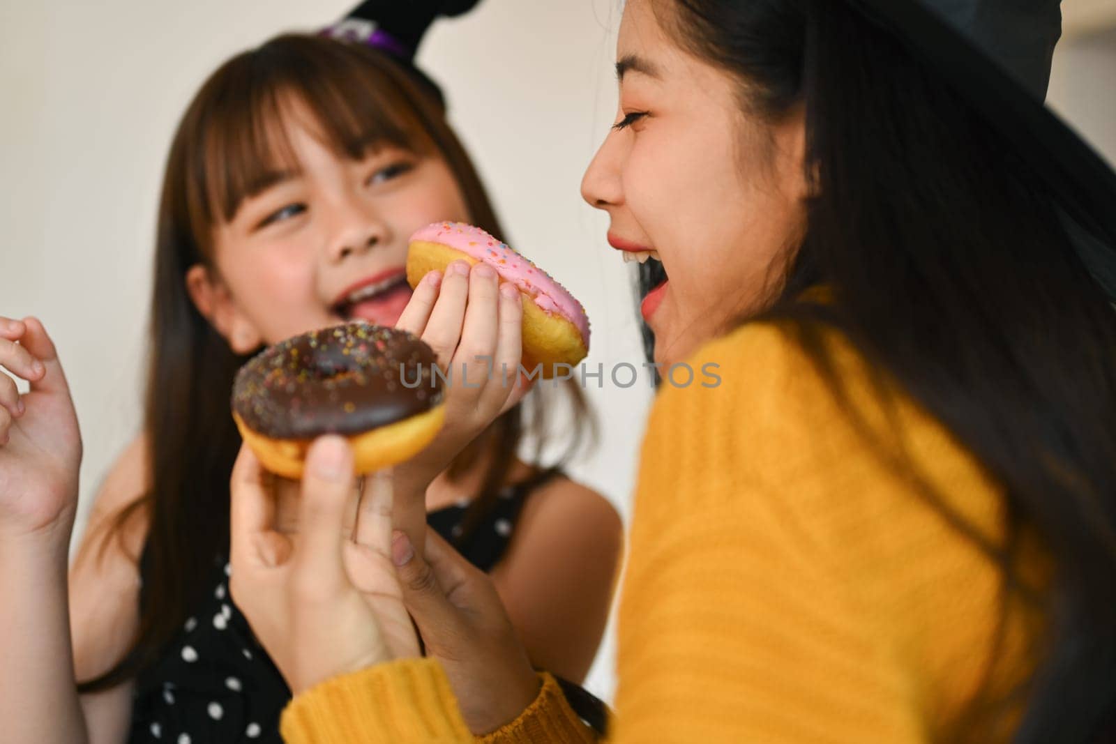 Happy family, cute little girl eating sweet donut with mother in kitchen. Halloween celebration and activity relationship in house.
