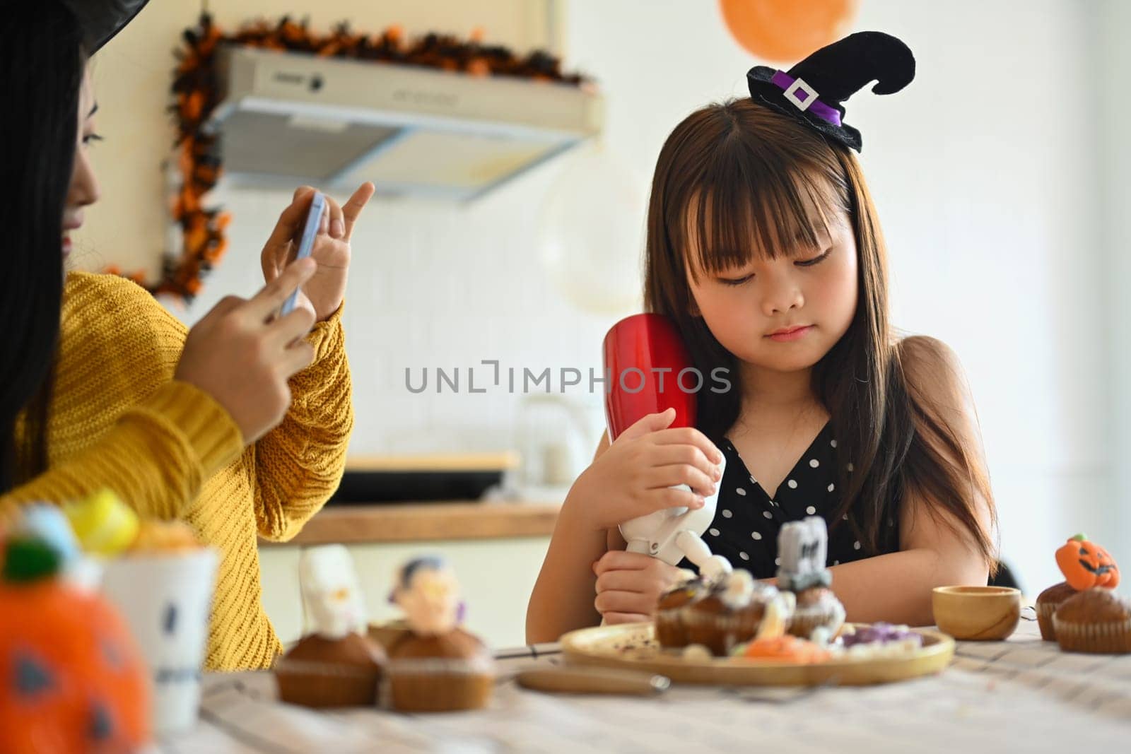 Happy mother and cute girl daughter are having fun preparing Halloween desserts in kitchen by prathanchorruangsak