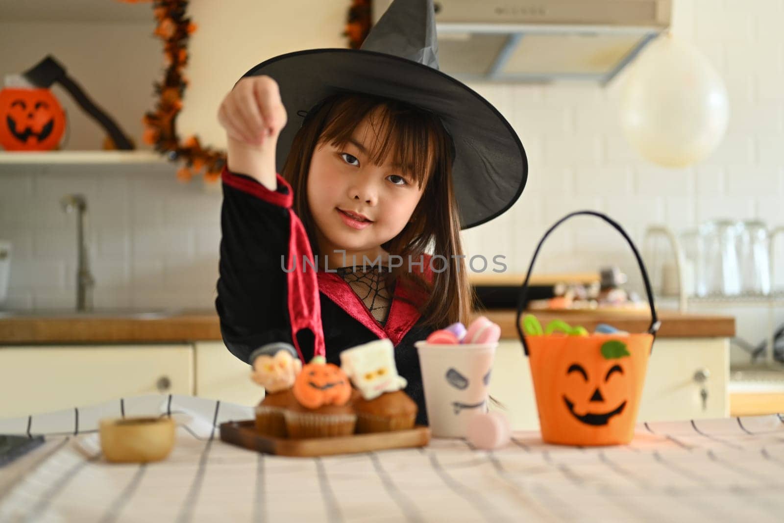 Adorable little girl decorating Halloween cupcakes with different monsters, pumpkins and ghosts by prathanchorruangsak