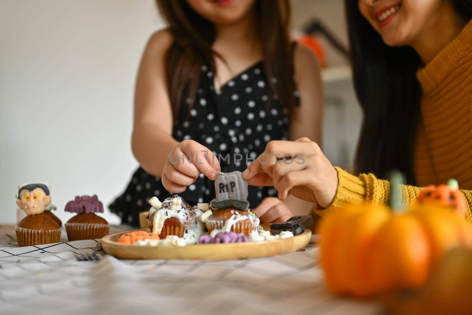 Cropped shot of little girl decorating Halloween cupcakes with different monsters, pumpkins and ghosts.