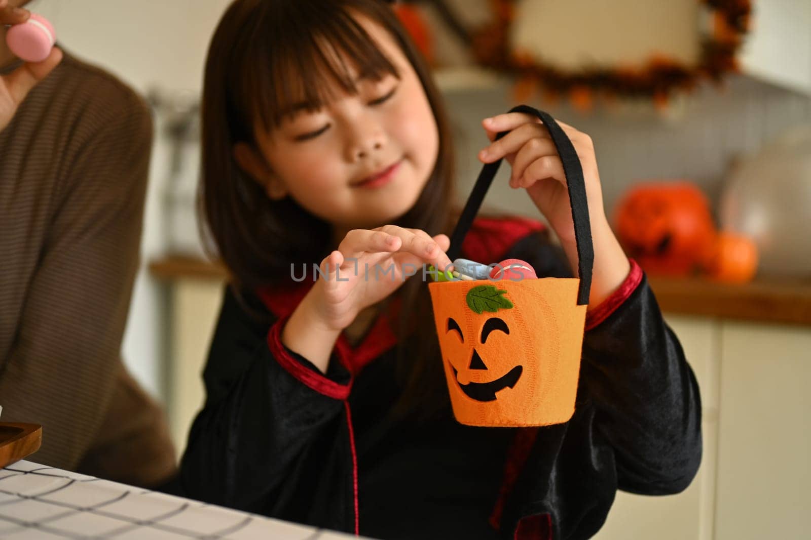 Cute little girl wearing Halloween costume holding pumpkin bucket with candies and sweets by prathanchorruangsak