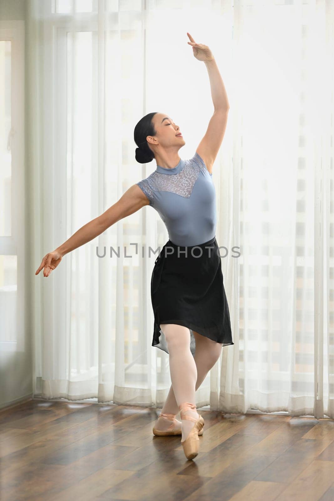 Full length beautiful ballerina dancing with graceful hands near window in studio. Dance, art and education concept by prathanchorruangsak