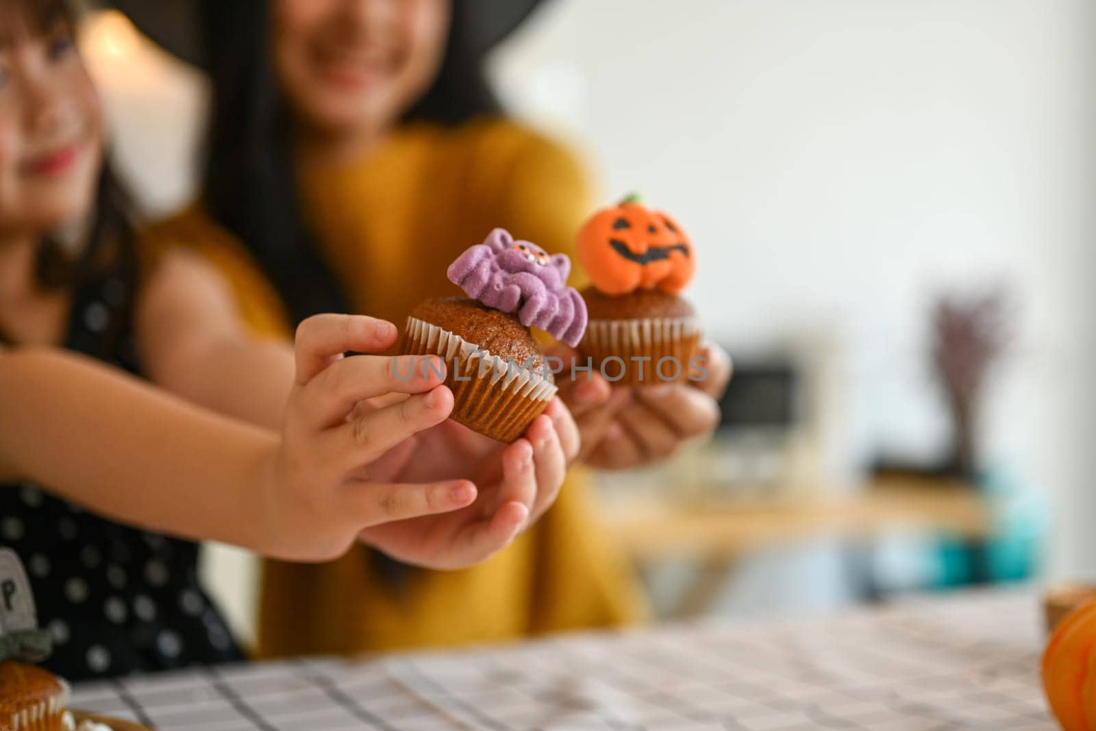 Close cup little girl and mother hands holding delicious Halloween cupcakes. Halloween celebration concept by prathanchorruangsak