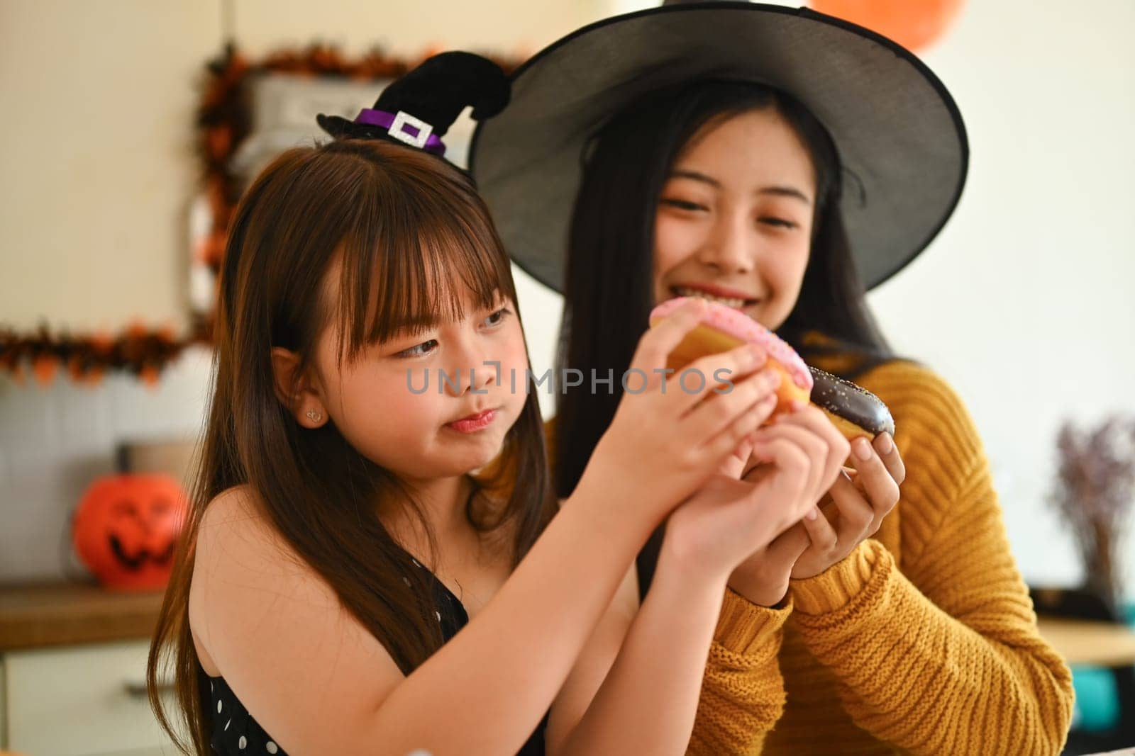 Happy mother and cute girl daughter are having fun preparing Halloween desserts in kitchen.