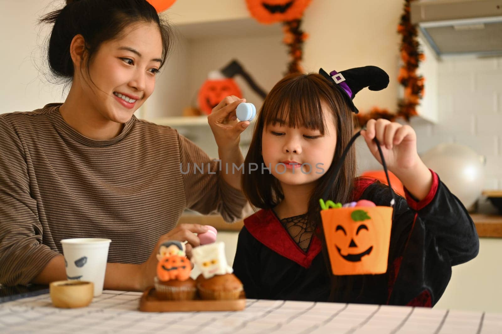 Smiling young mother and her little daughter getting ready for the holiday, making Halloween cupcakes by prathanchorruangsak
