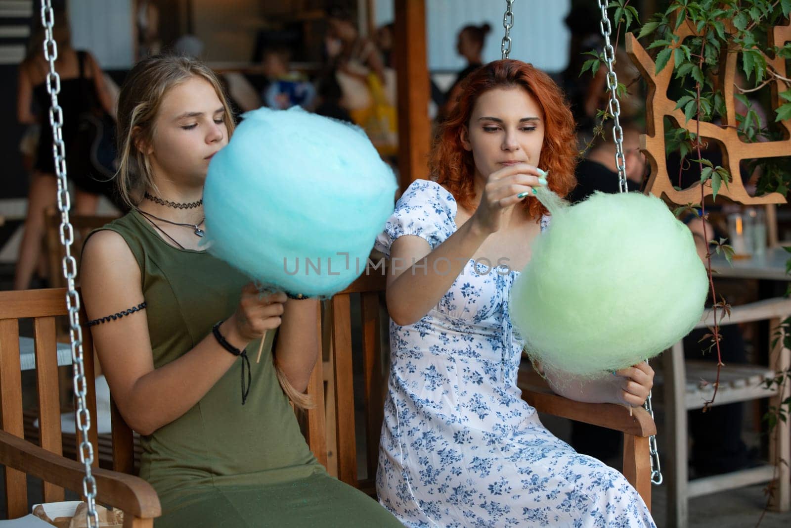 Two friends happily savoring colorful cotton candy together outdoors, capturing a joyful and vibrant summer moment