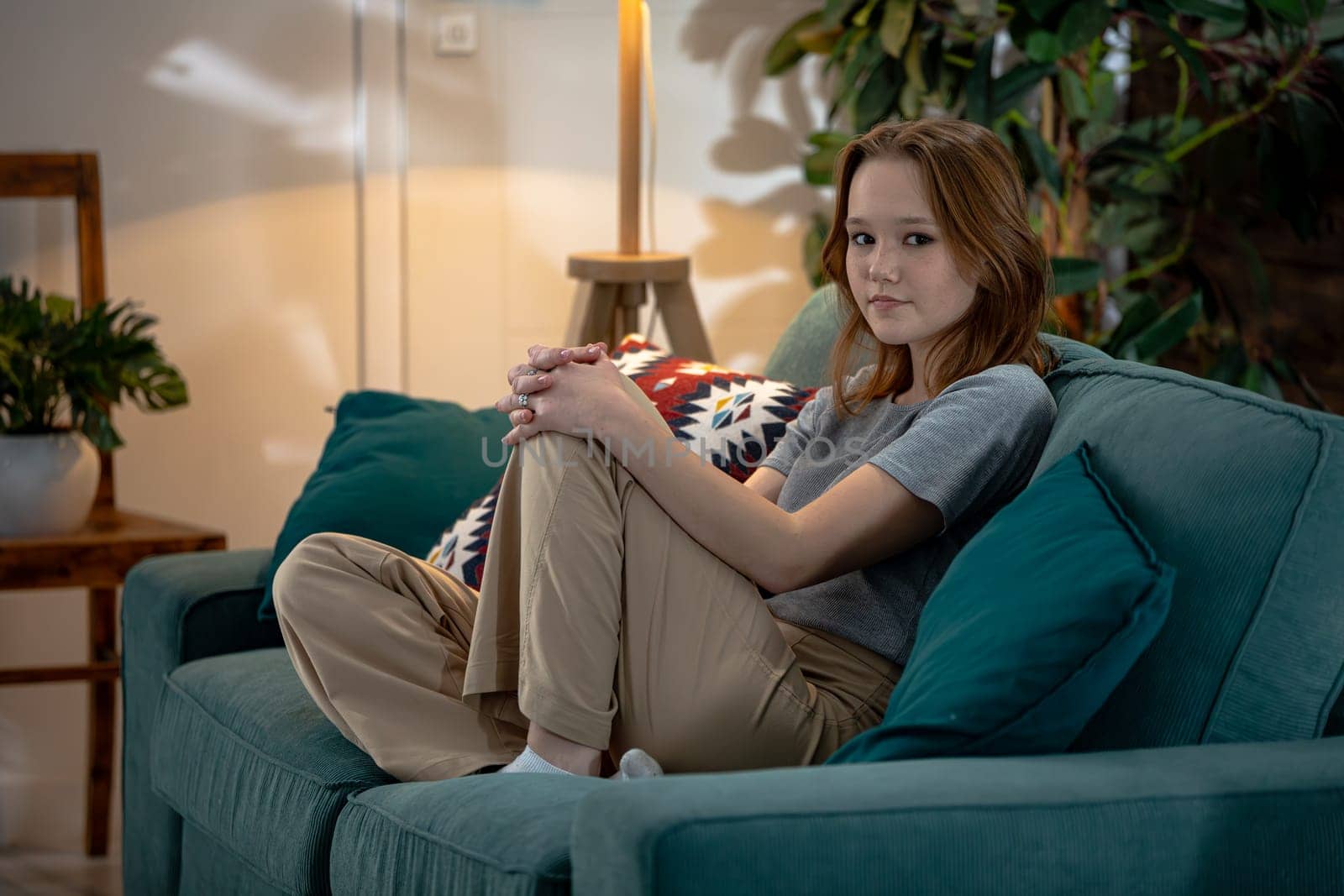 A thoughtful young woman sits comfortably on a cozy couch, enveloped in warm surroundings that evoke deep introspection