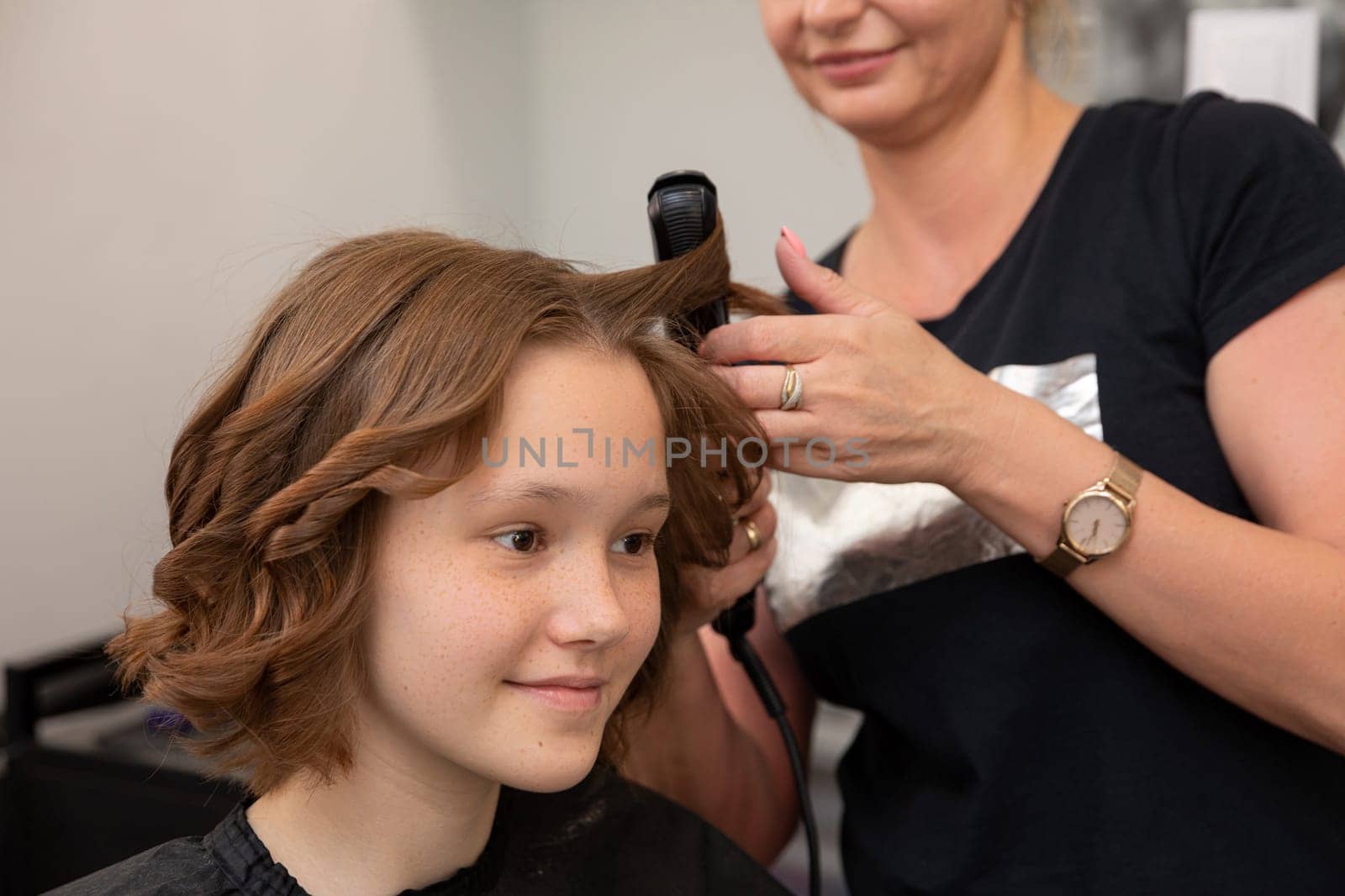 A young girl is having a delightful and stylish hair curling session at a topnotch, professional salon