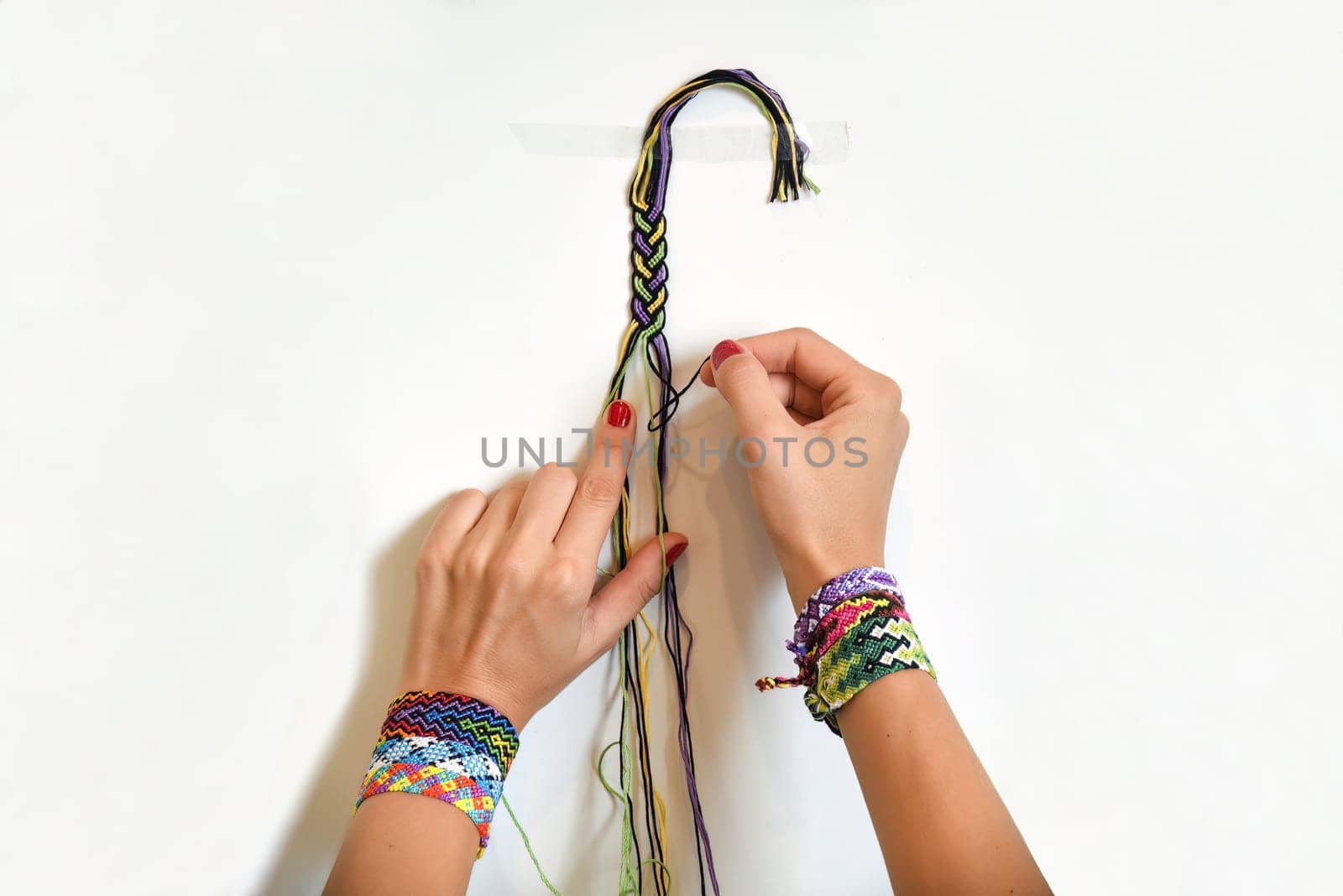 Female hands weaving knot for DIY friendship bracelet Pigtail. Many handmade bracelets on girls wrists. Friendship bracelet making process, step by step. White background with copy space