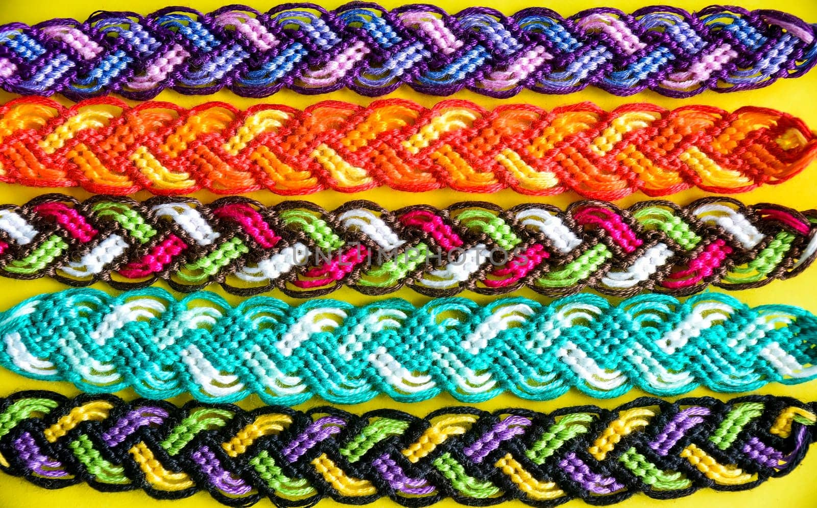 Selective focus of multi-colored woven DIY friendship bracelets Pigtail handmade of embroidery bright thread with knots on yellow background