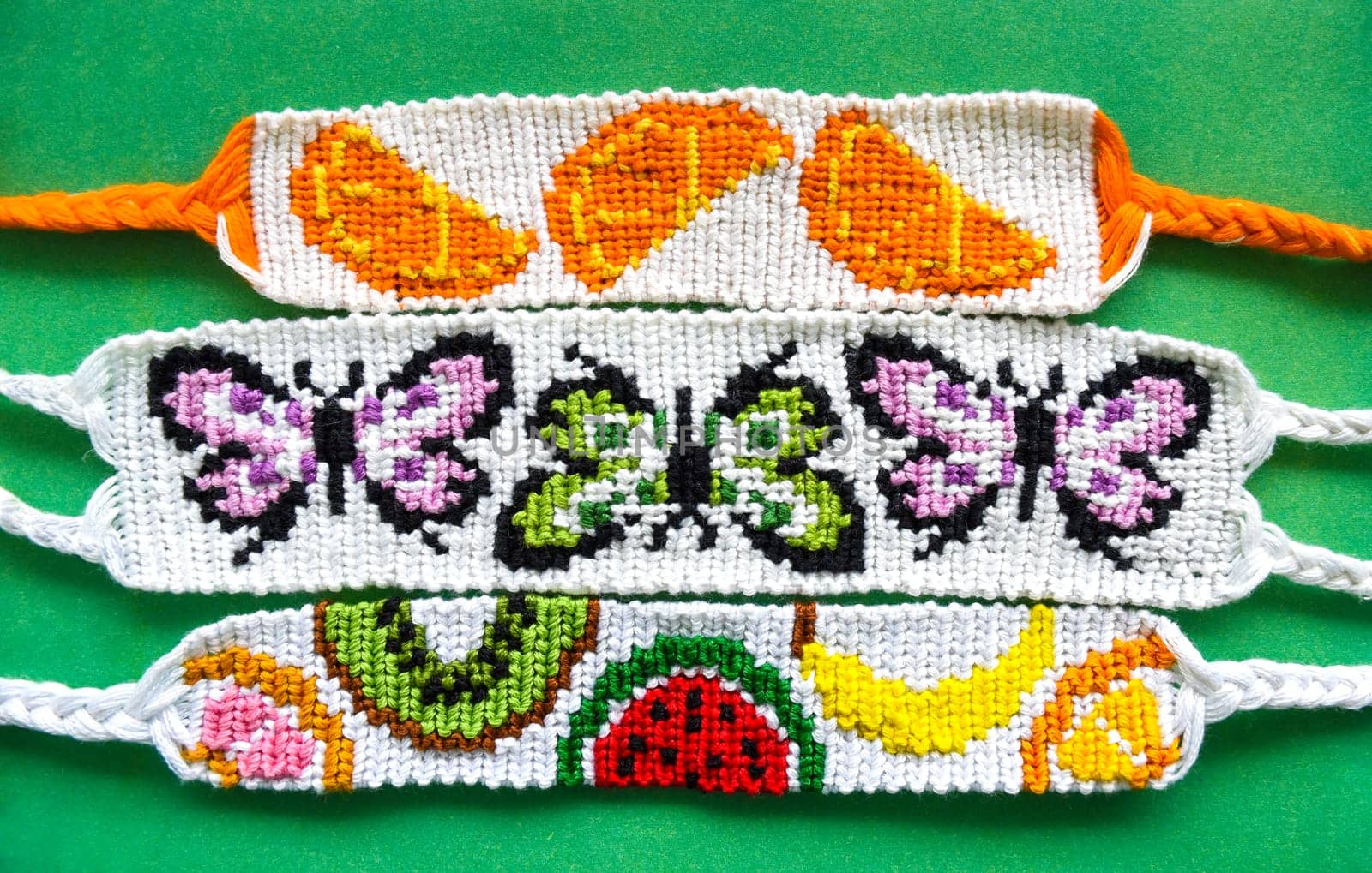 Three white woven DIY friendship bracelets handmade of embroidery bright thread with knots. Alpha weaving with fruit and butterflies patterns