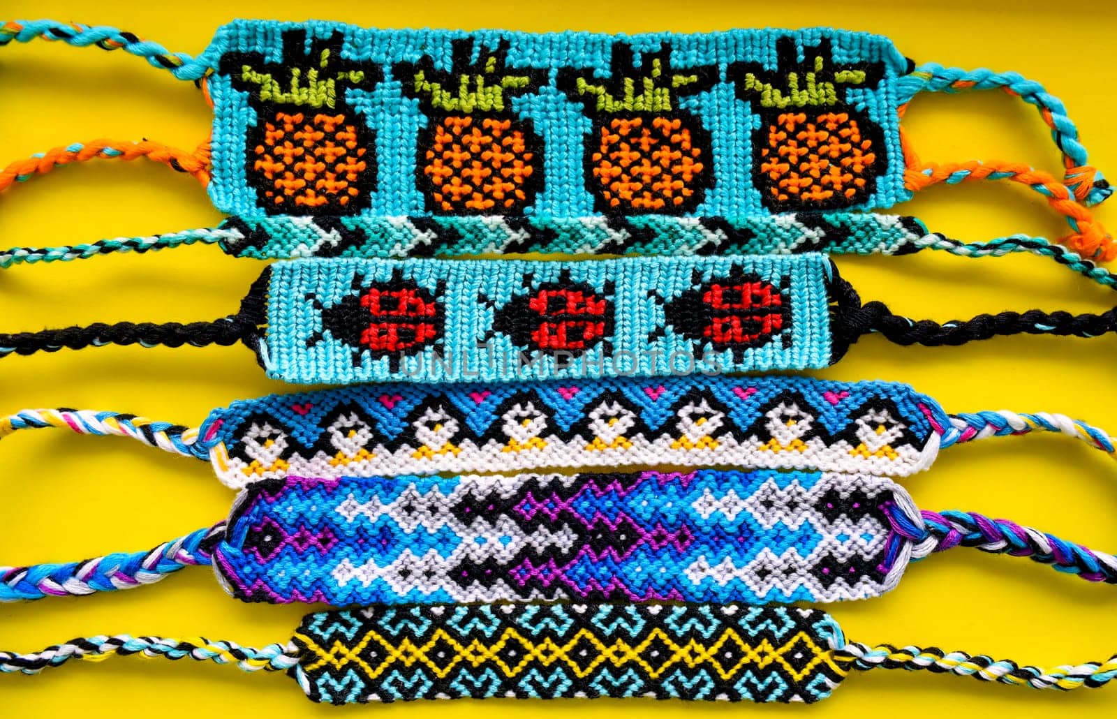 Many tied woven DIY friendship bracelets handmade of embroidery bright thread with knots on yellow background. Alpha and normal patterns
