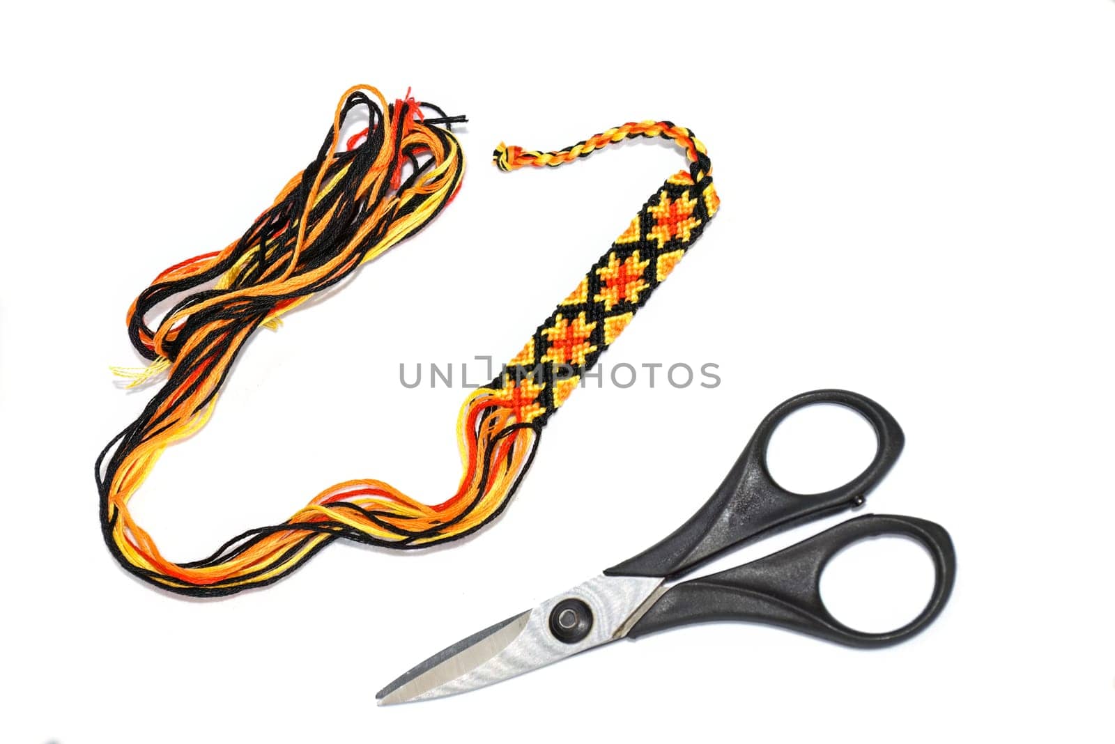 Unfinished woven DIY friendship bracelet with boho pattern next to scissors on white background