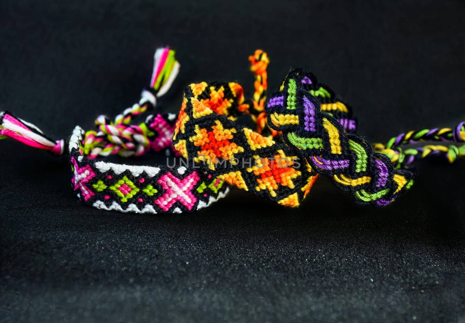 Woven DIY friendship bracelets handmade of embroidery bright thread with knots on black background.