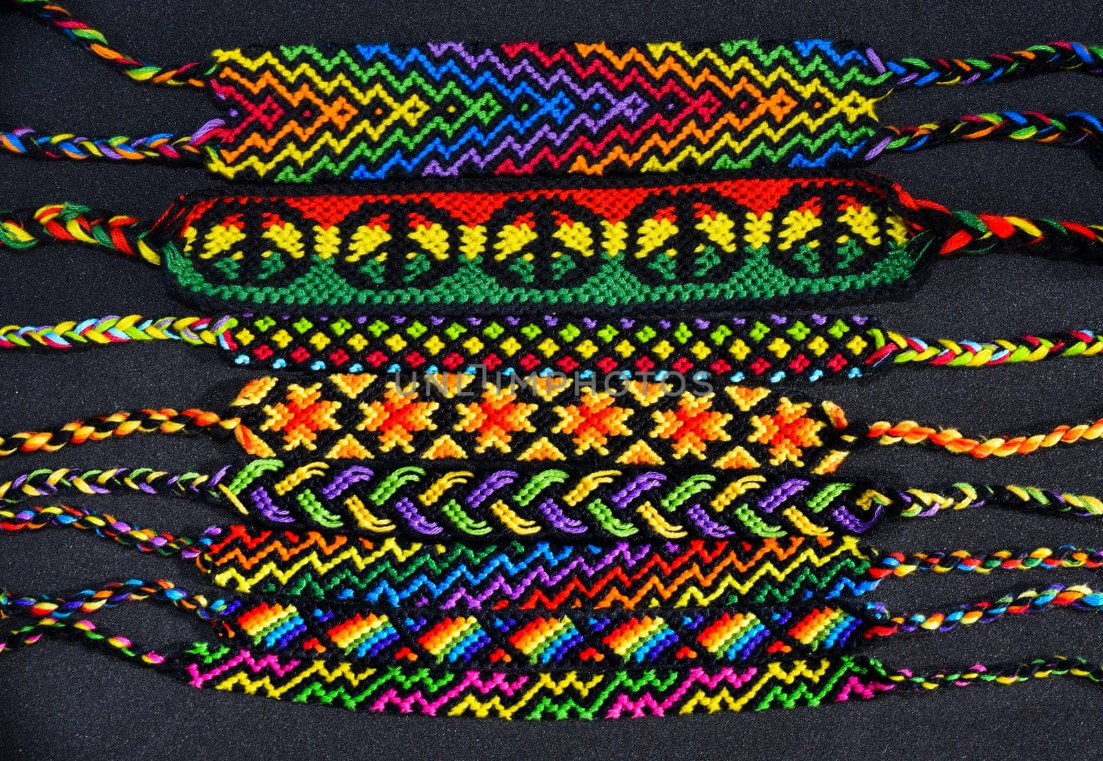 Woven DIY friendship bracelets handmade of embroidery bright thread with knots on black background.