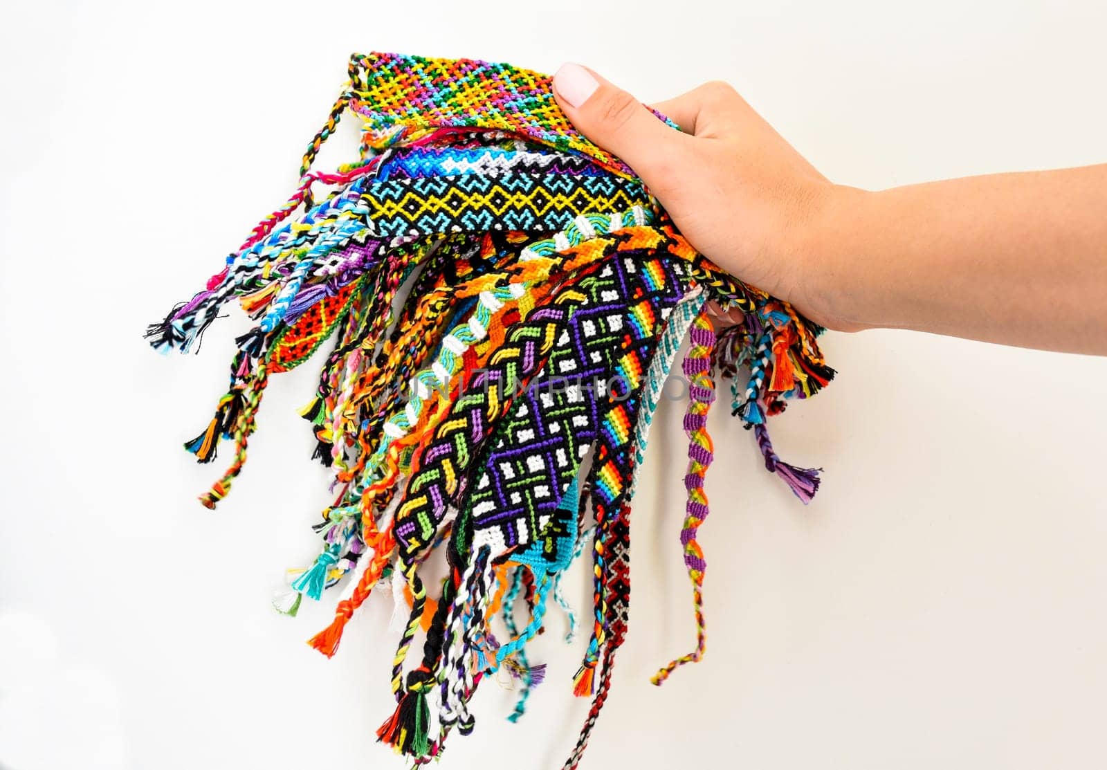 Female hand holding many woven multi-colored DIY friendship bracelets handmade of embroidery thread with knots on white background.
